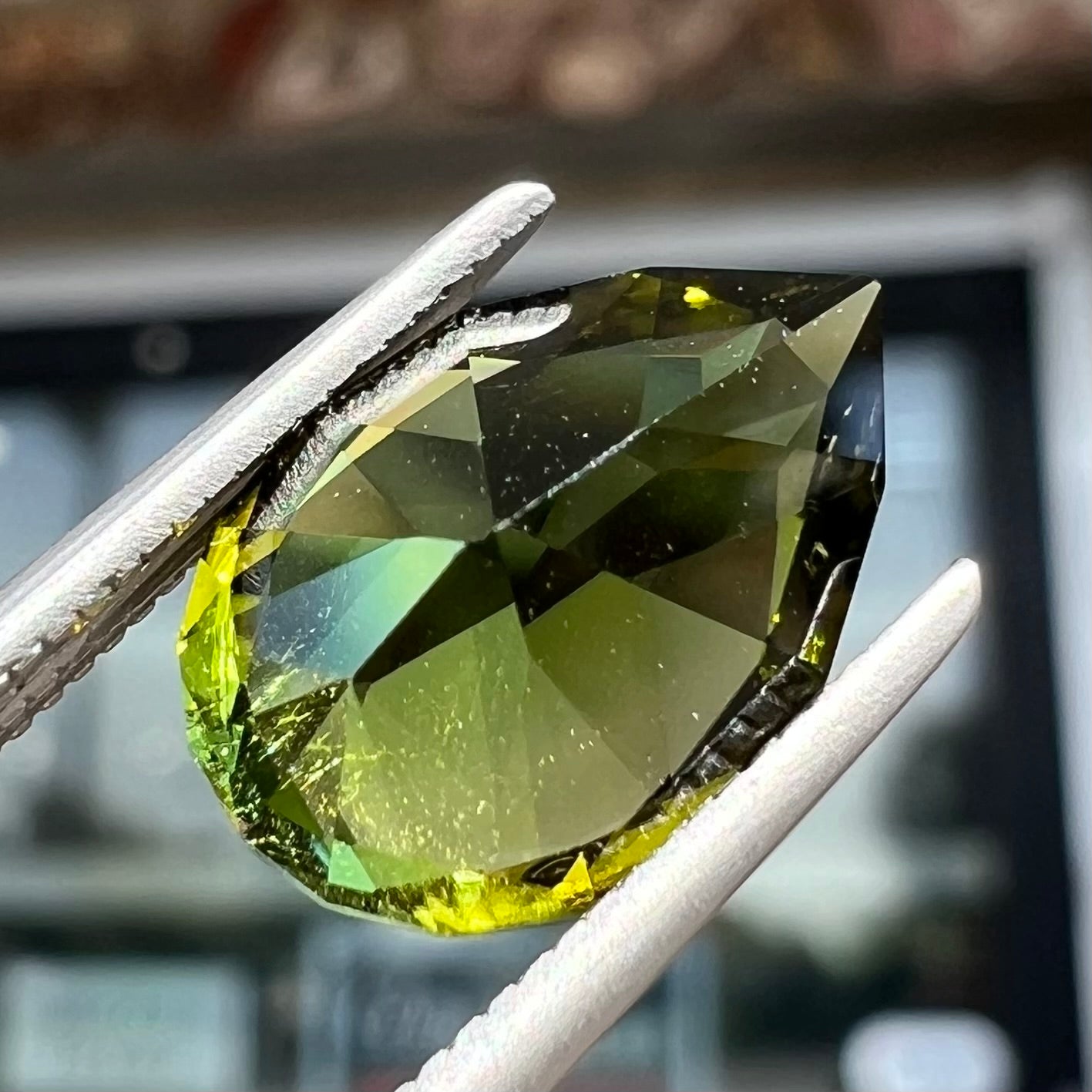 A loose, pear shaped green tourmaline gemstone. The color is dark green with a yellow secondary hue.