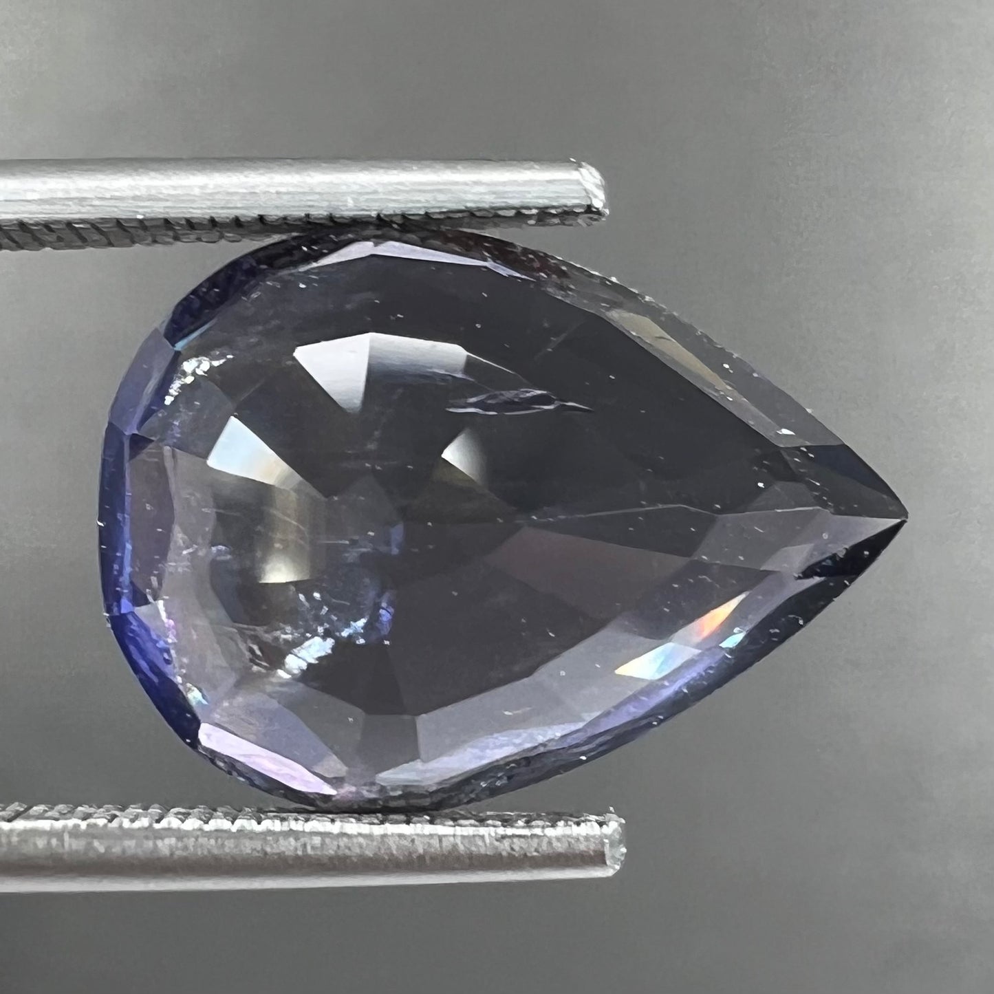 A loose, pear shaped bicolor iolite gemstone. The stone shows violite purple and silver colors.