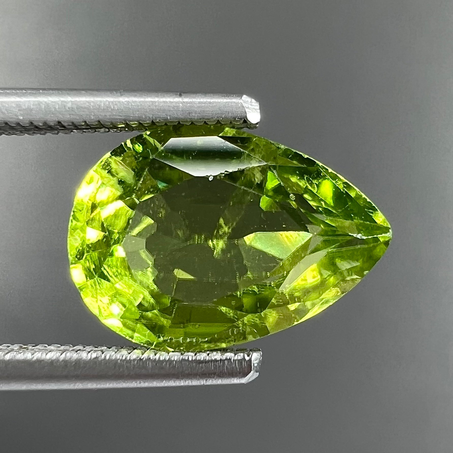 A loose, yellow green, pear shaped peridot gemstone.