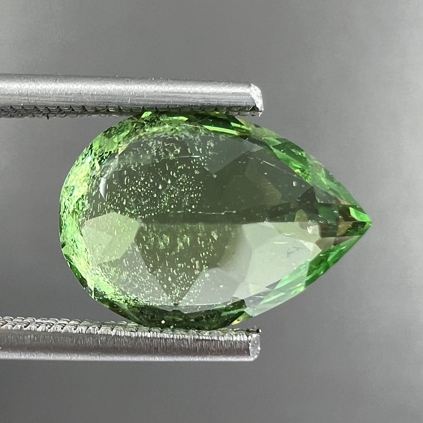 A loose, pear shaped tsavorite garnet gemstone. The stone is yellowish green.