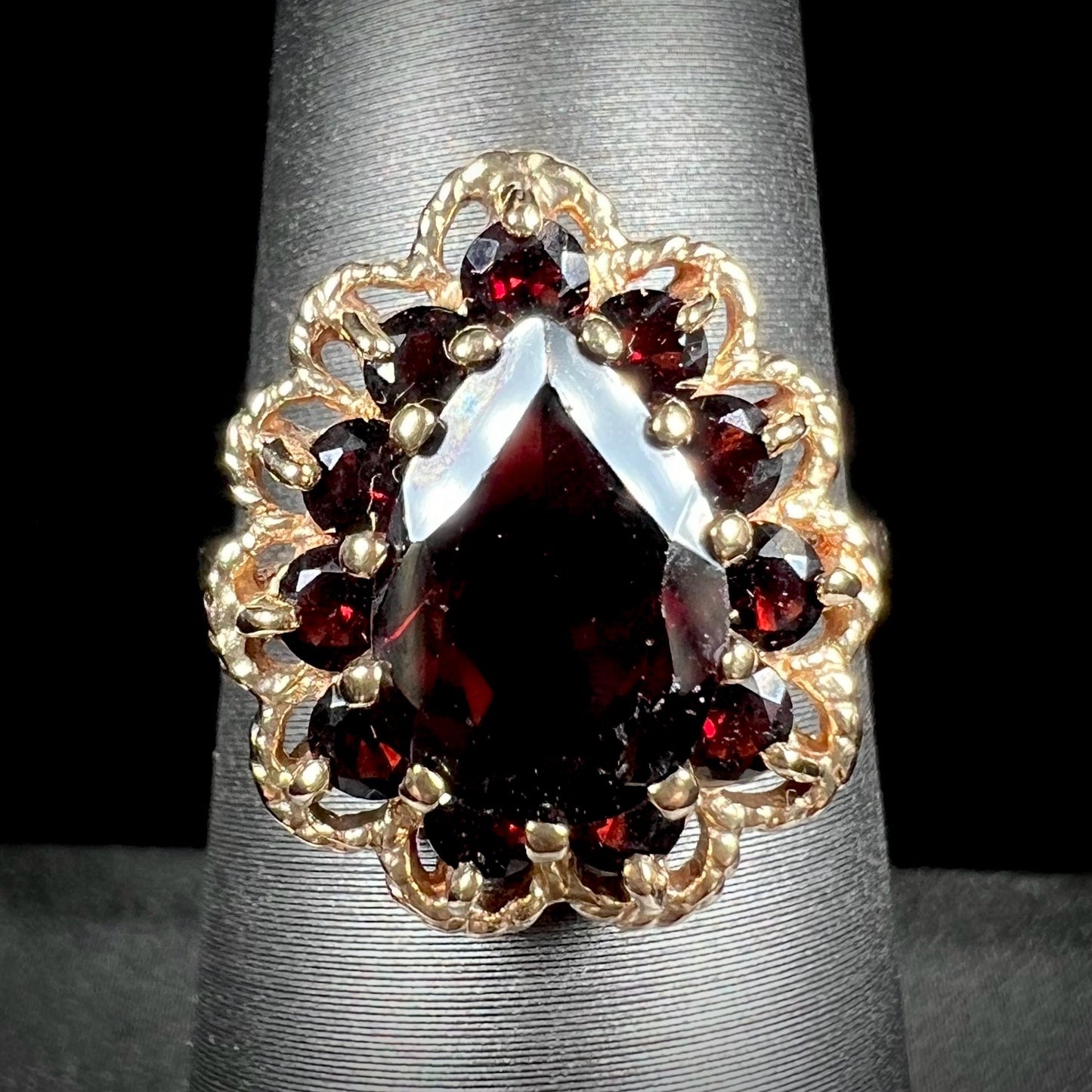 A vintage, 1940's style yellow gold ring set with a pear shaped almandine garnet. A halo of round garnets surround the center stone.