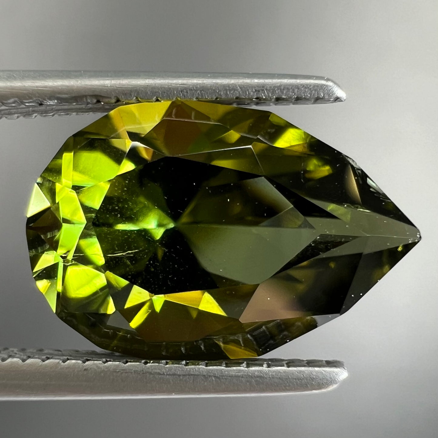 A loose, pear shaped green tourmaline gemstone. The color is dark green with a yellow secondary hue.