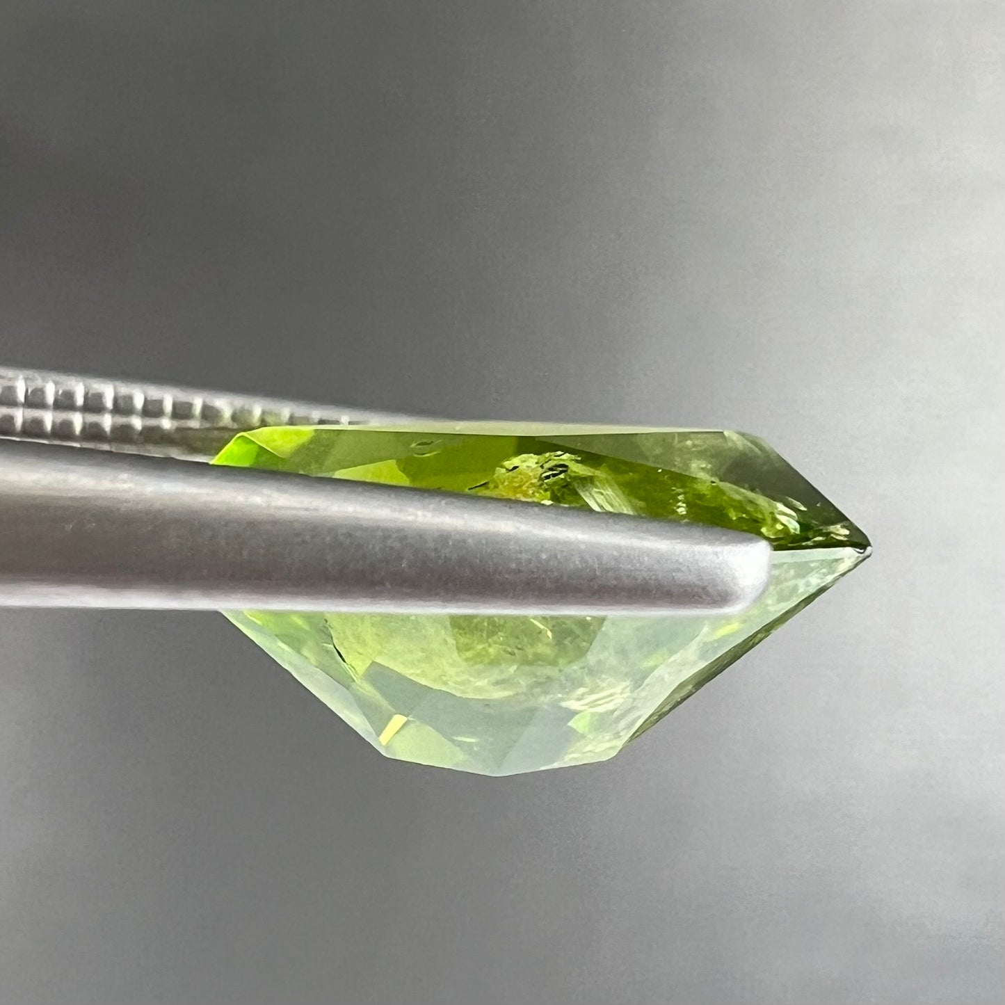 A loose, modified octagon peridot stone. The stone is a yellow green color.