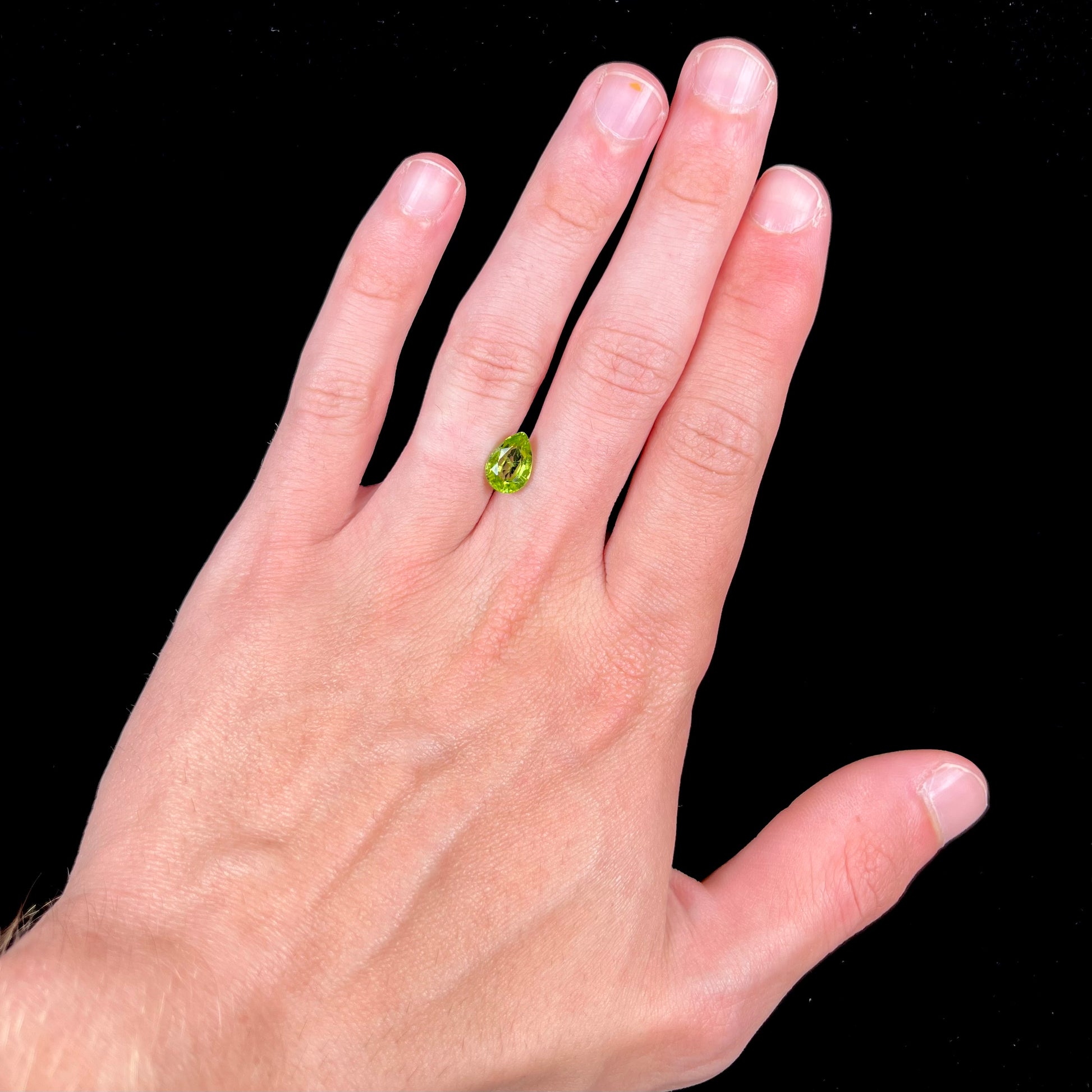 A loose, yellow green, pear shaped peridot gemstone.