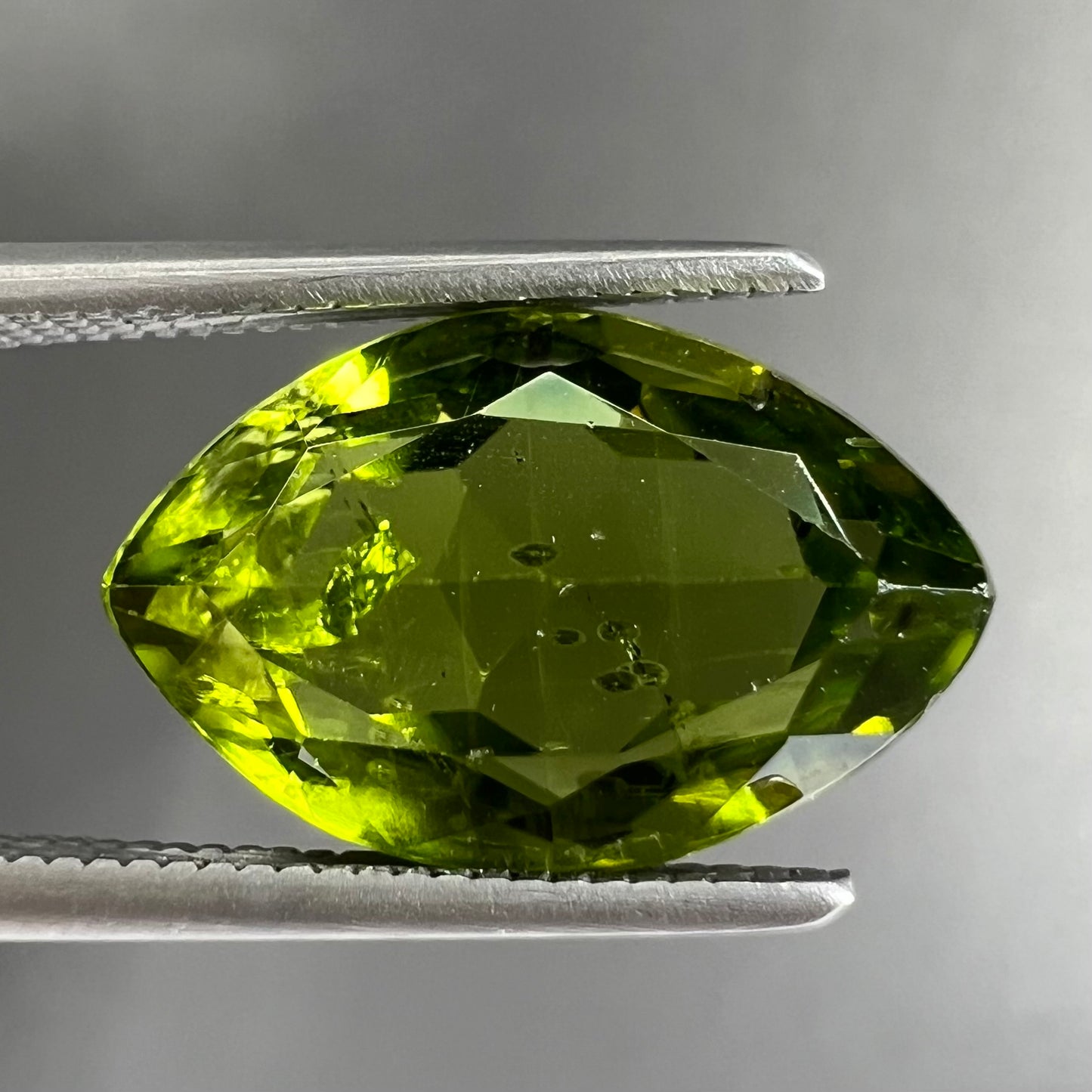 A loose, marquise cut peridot gemstone. The stone is an olive green color.