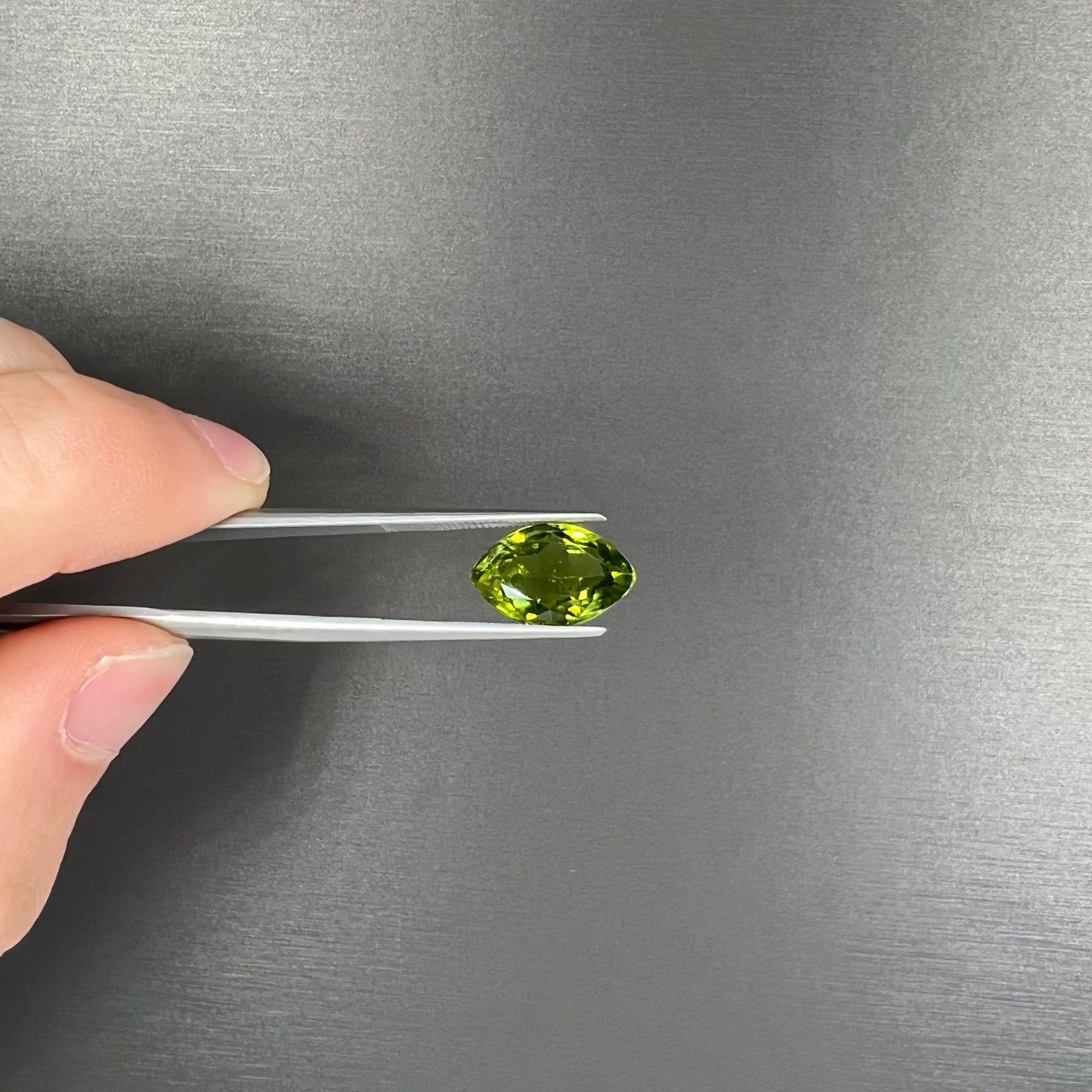 A loose, marquise cut peridot gemstone. The stone is an olive green color.