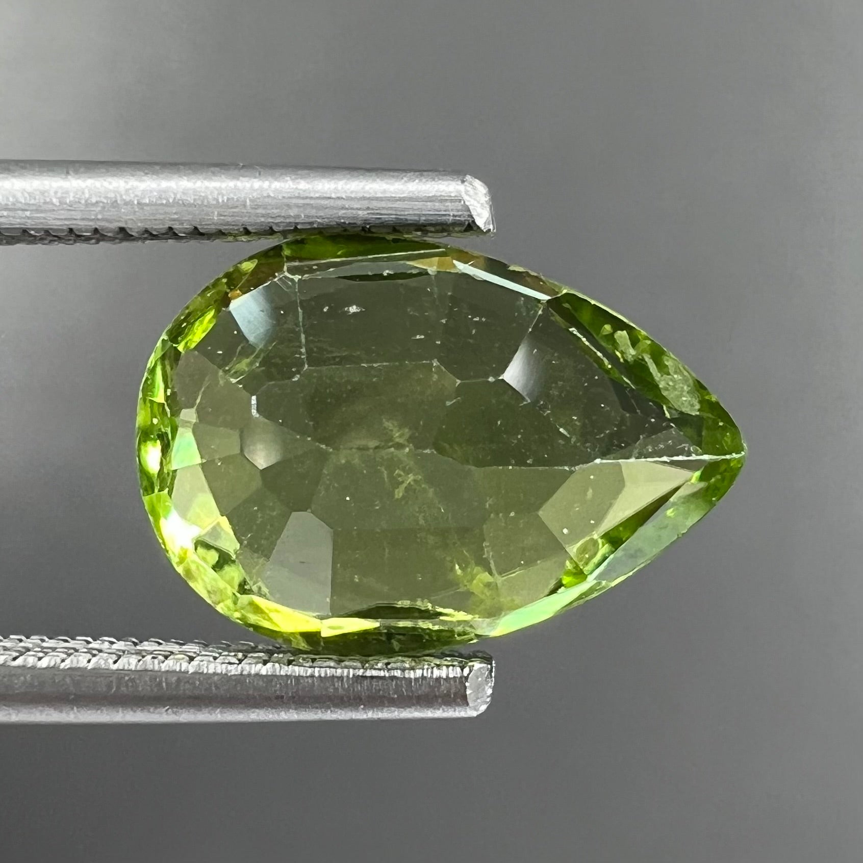 A loose, yellow green, pear shaped peridot gemstone.
