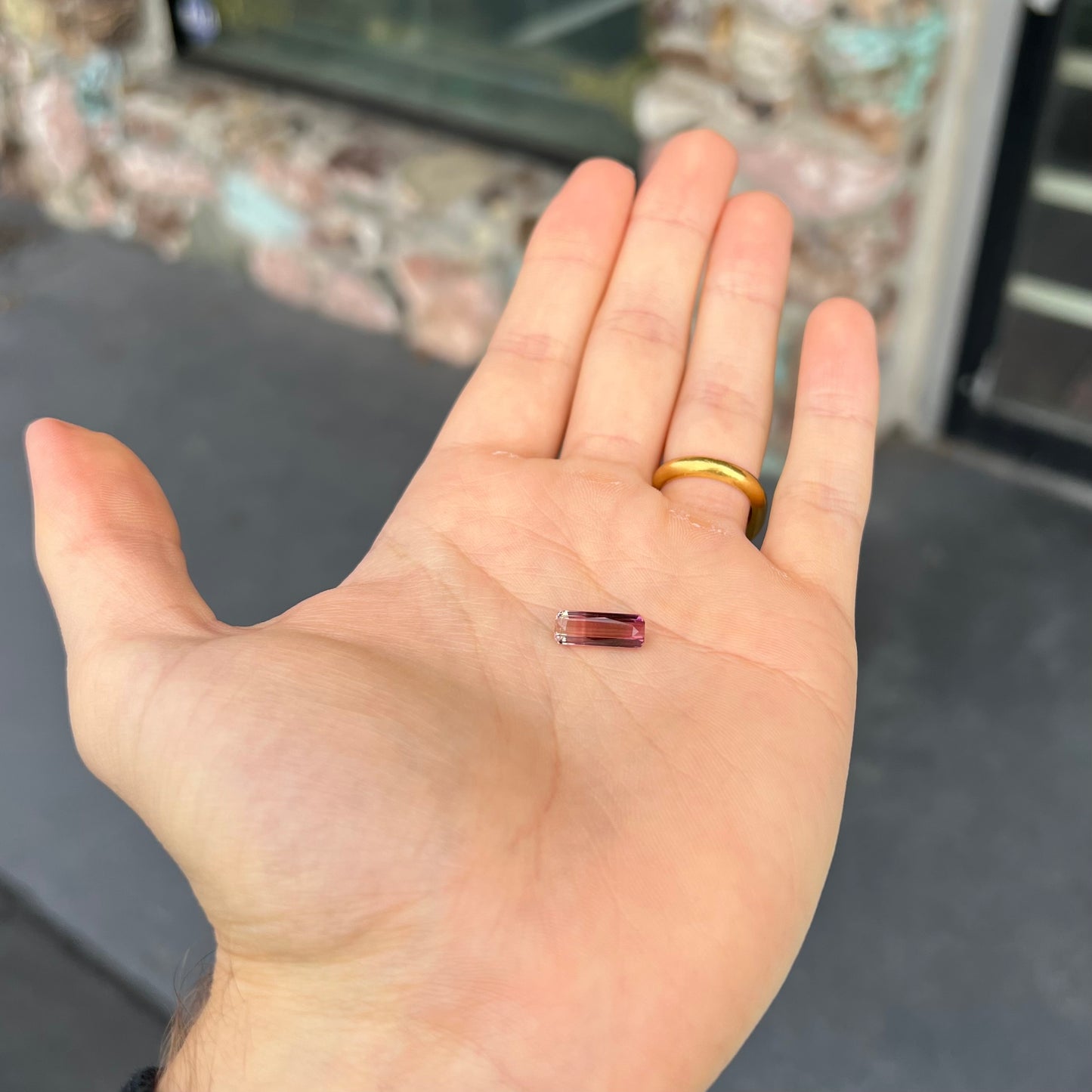 A loose, modified emerald cut tricolor tourmaline. The stone transitions from pink to light pink to white colors.