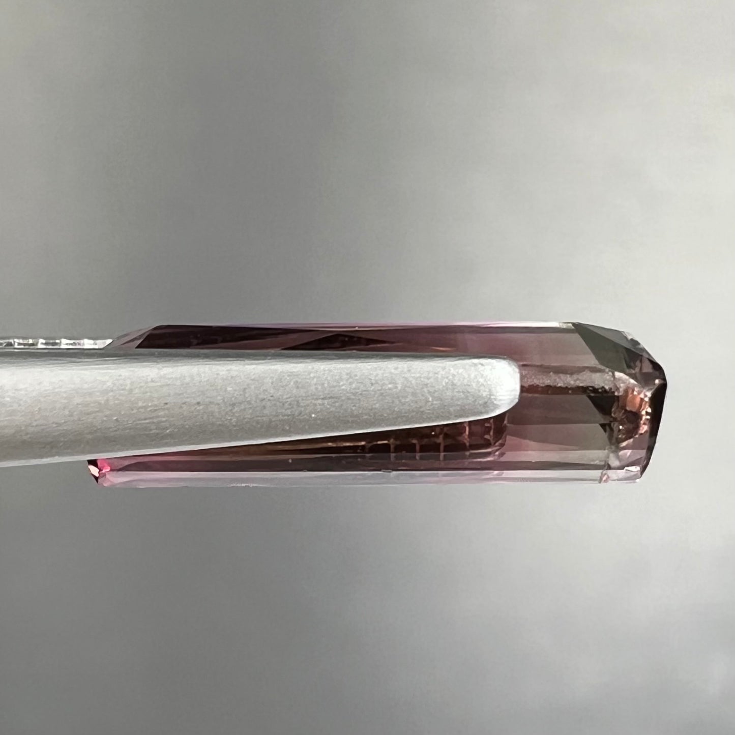 A loose, modified emerald cut tricolor tourmaline. The stone transitions from pink to light pink to white colors.