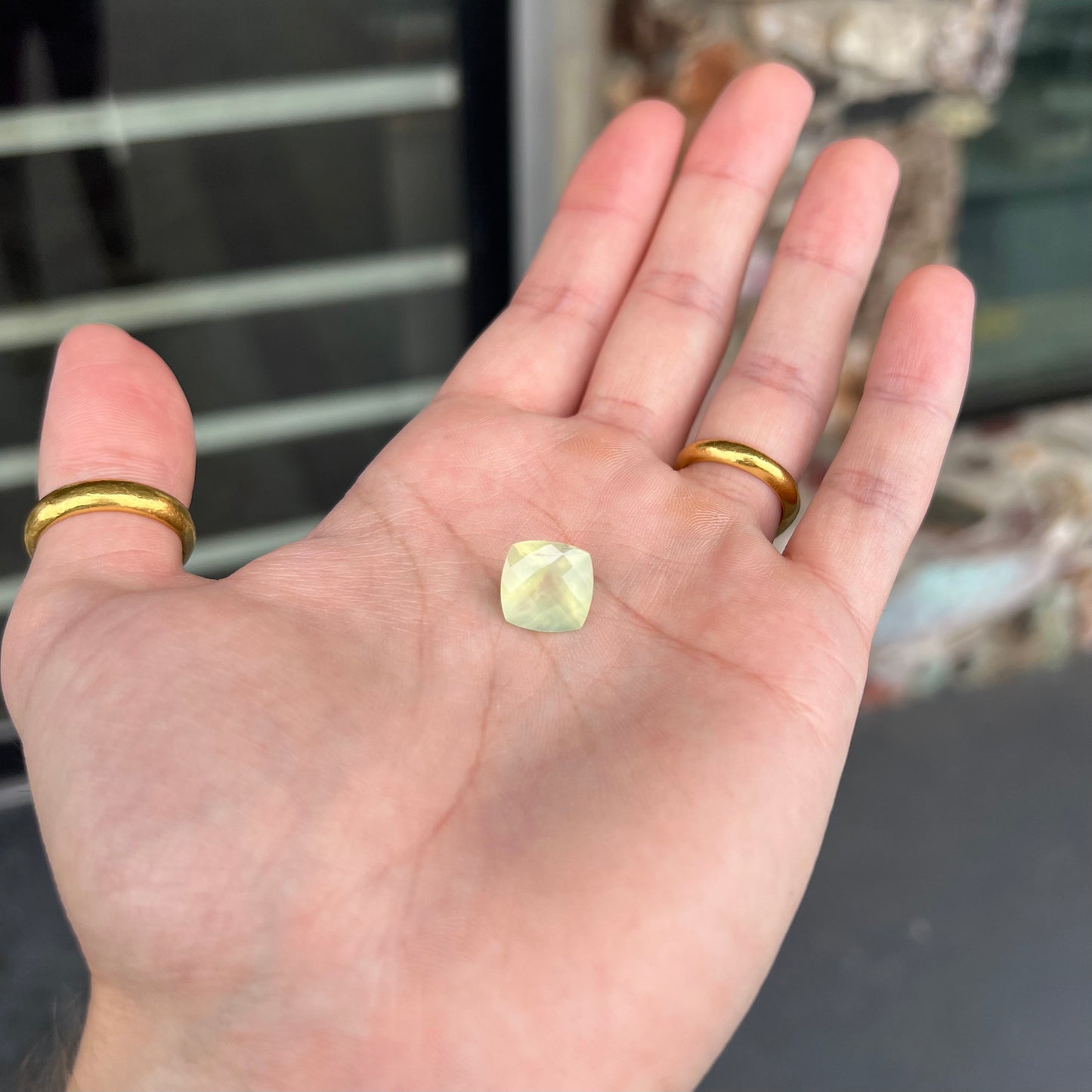 A loose, faceted checkerboard cushion cut green prehnite stone. The stone is sleepy yellowish green.