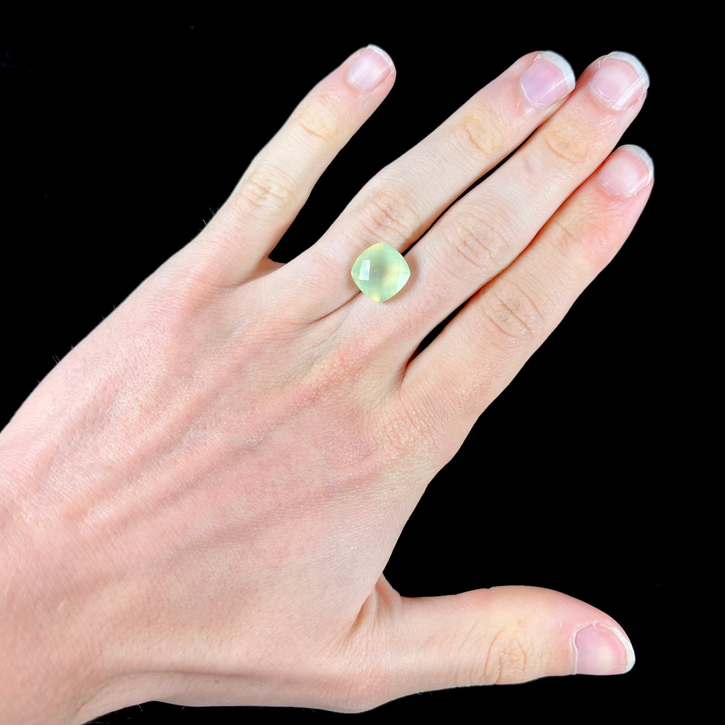 A loose, checkerboard cushion cut prehnite gemstone. The stone is a sleepy yellow green color.