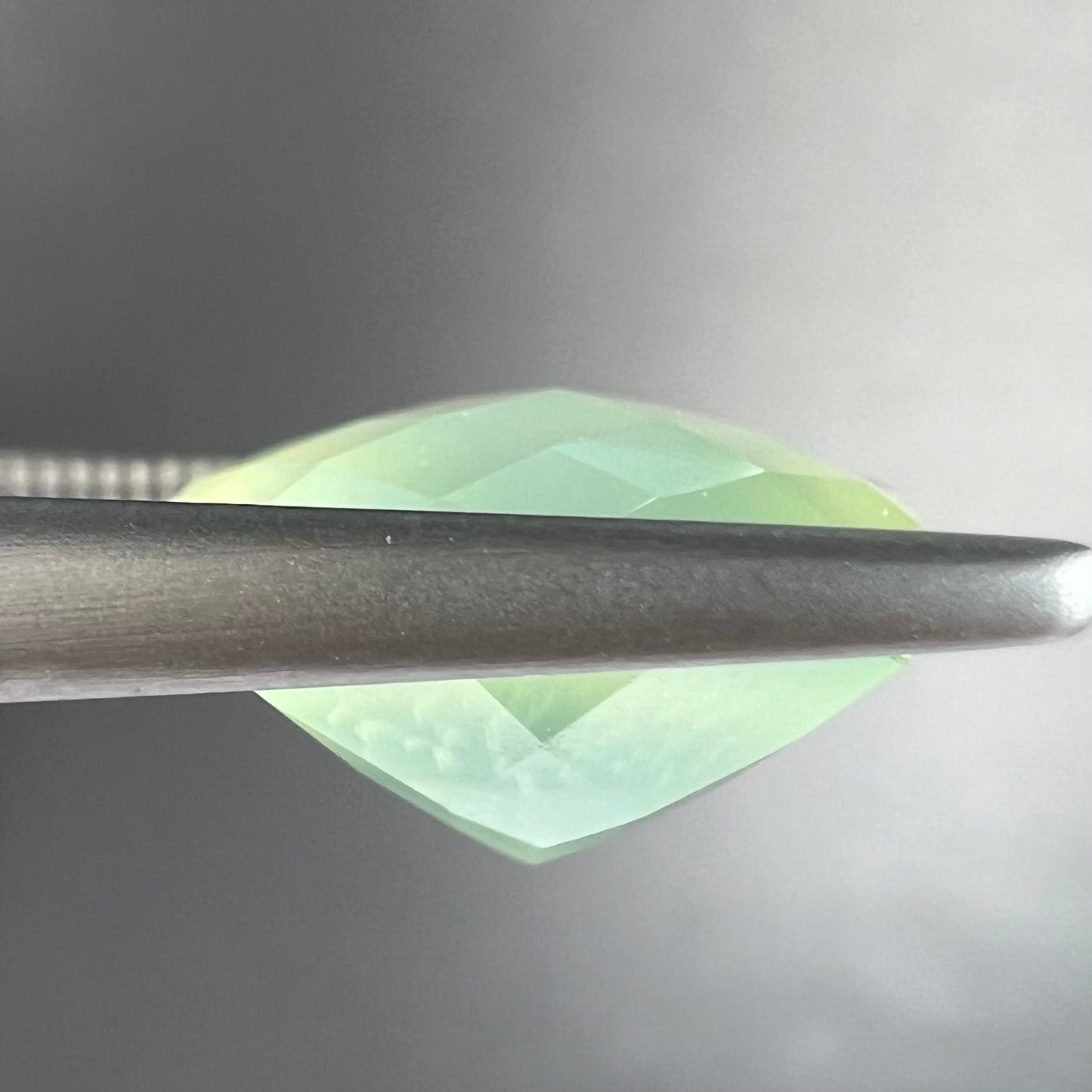 A loose, checkerboard cushion cut prehnite gemstone. The stone is a sleepy yellow green color.
