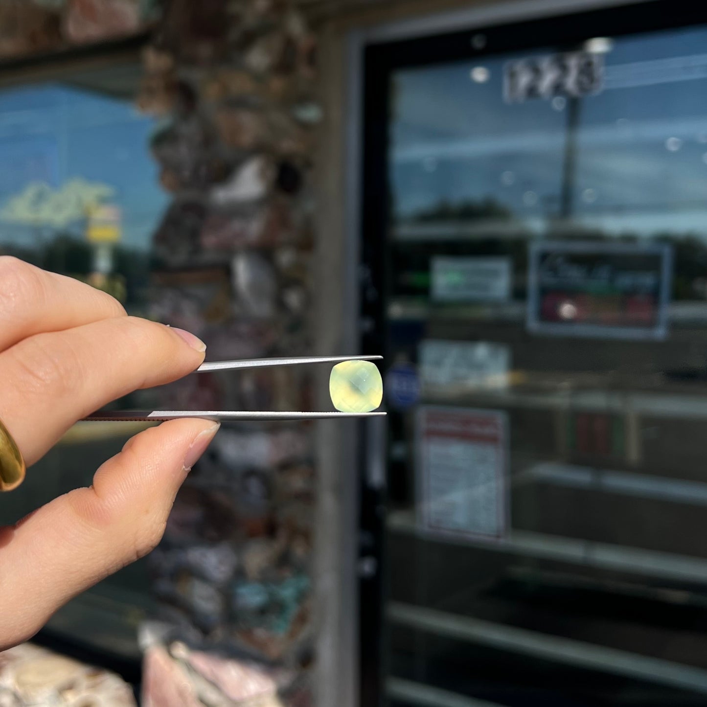 A loose, checkerboard cushion cut prehnite gemstone. The stone is a sleepy yellow green color.