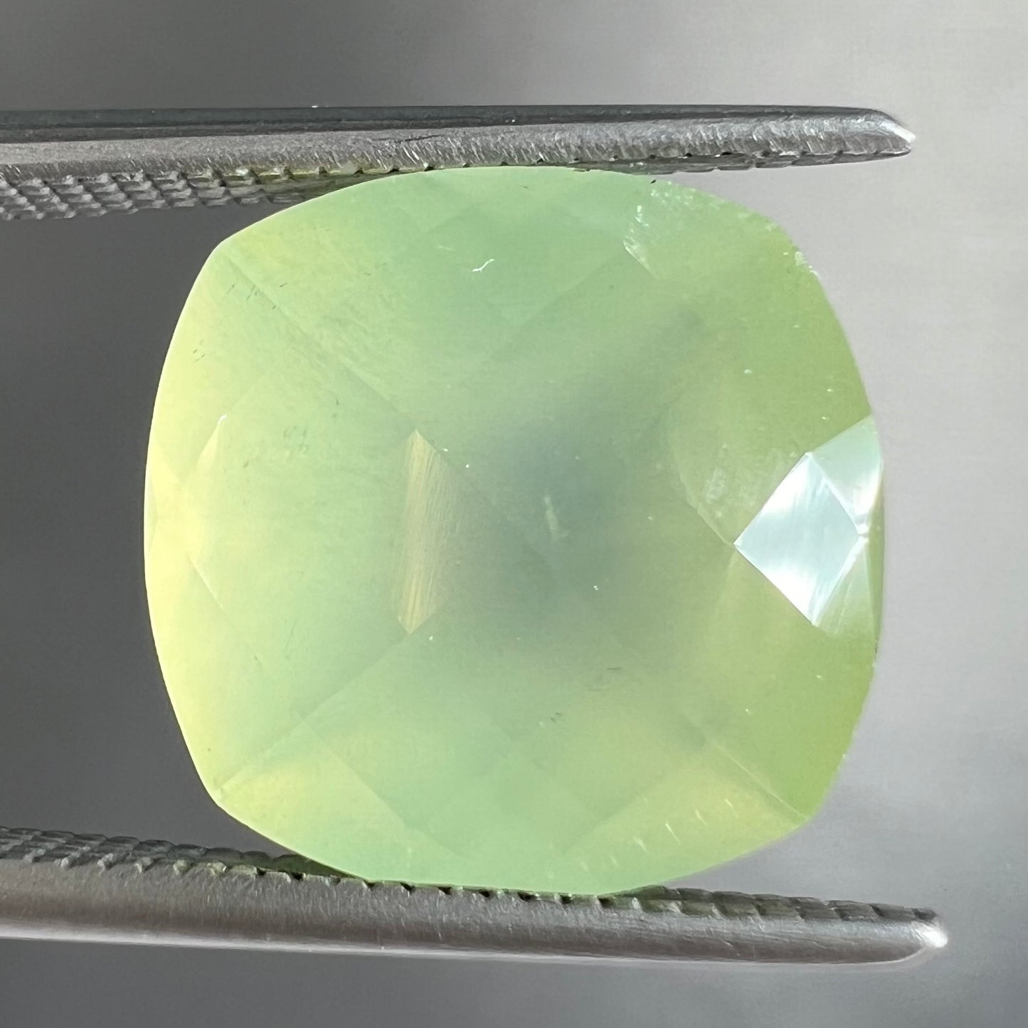 A loose, checkerboard cushion cut prehnite gemstone. The stone is a sleepy yellow green color.