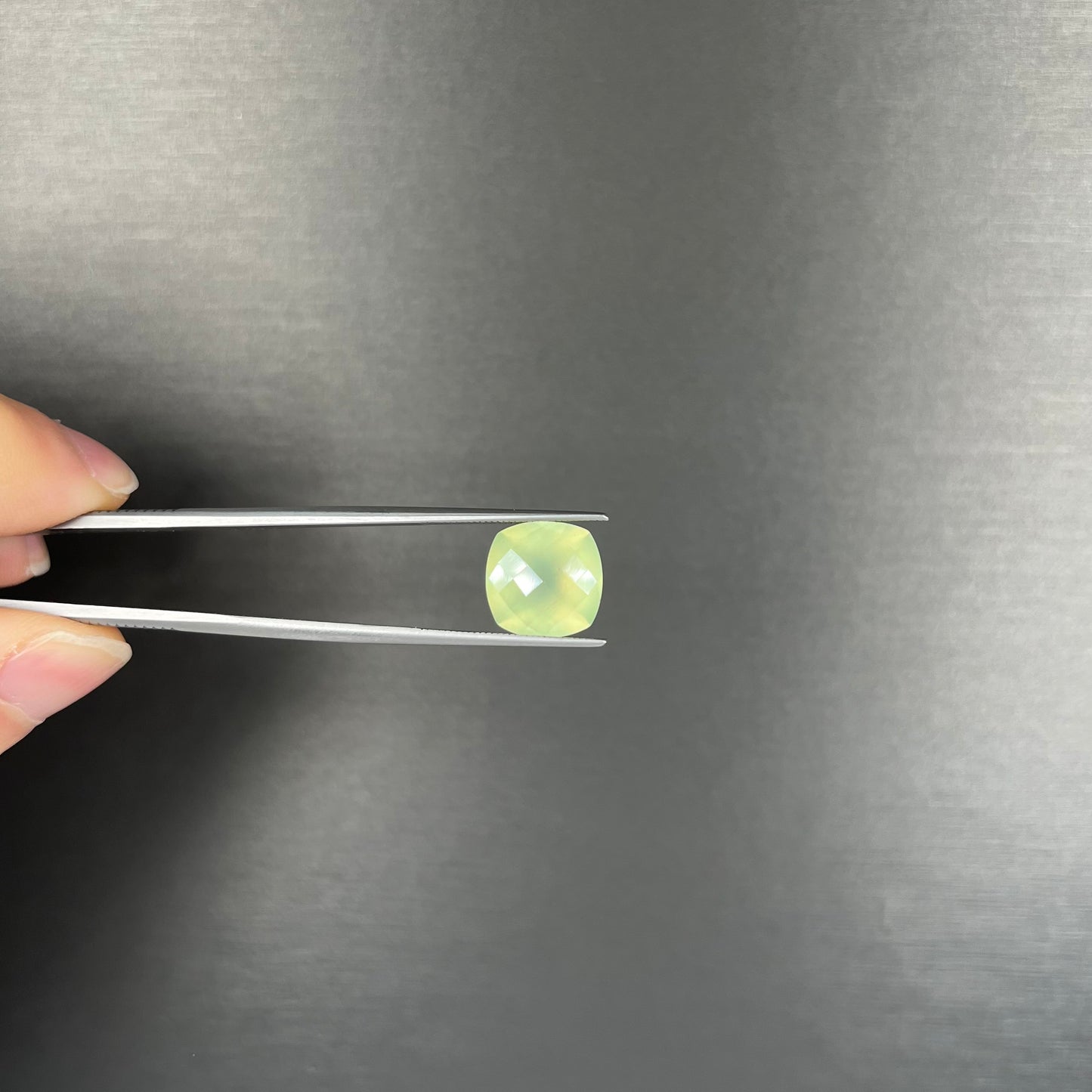 A loose, checkerboard cushion cut prehnite gemstone. The stone is a sleepy yellow green color.