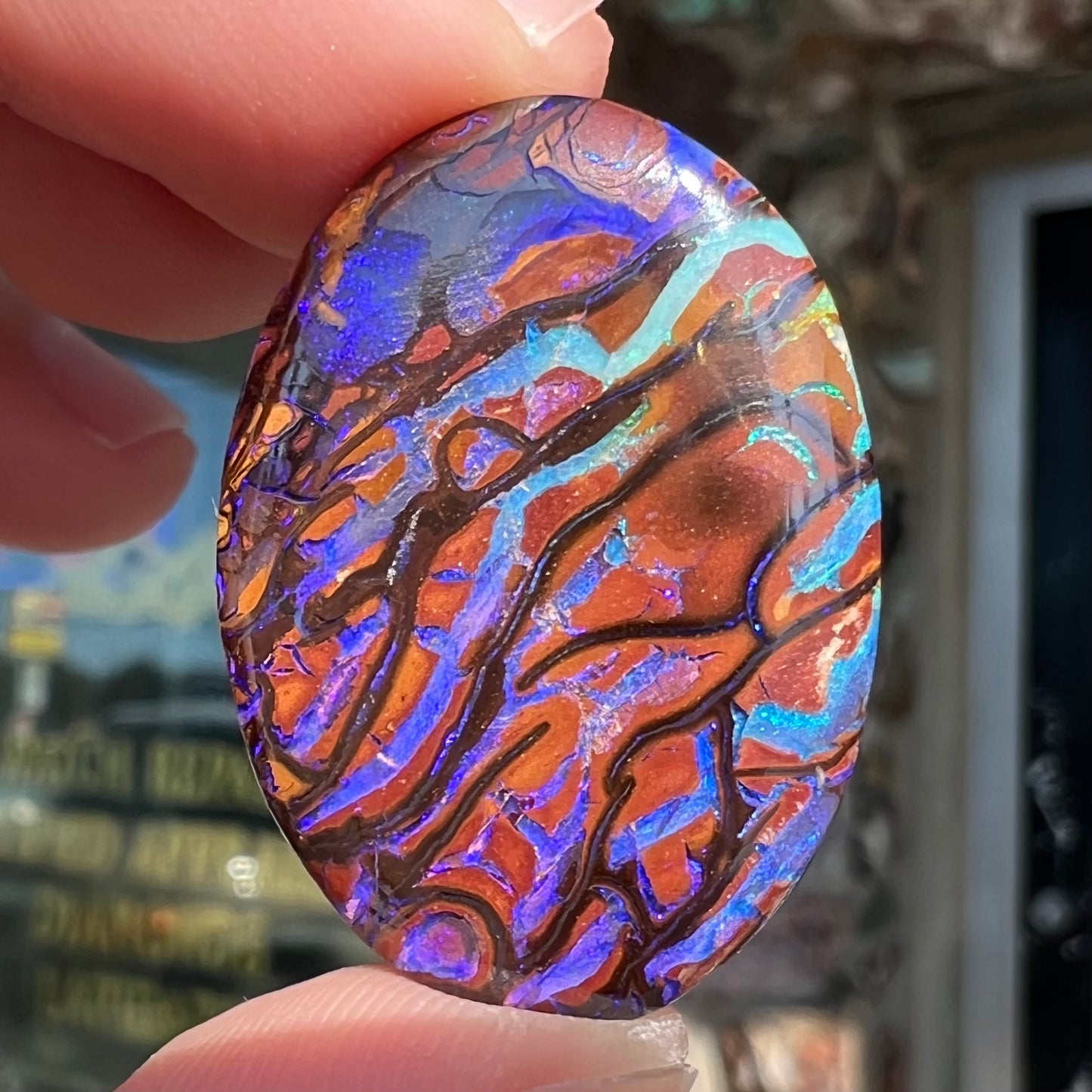 A loose, oval cabochon cut boulder opal from Koroit, Australia. The opal has violet and purple veins.