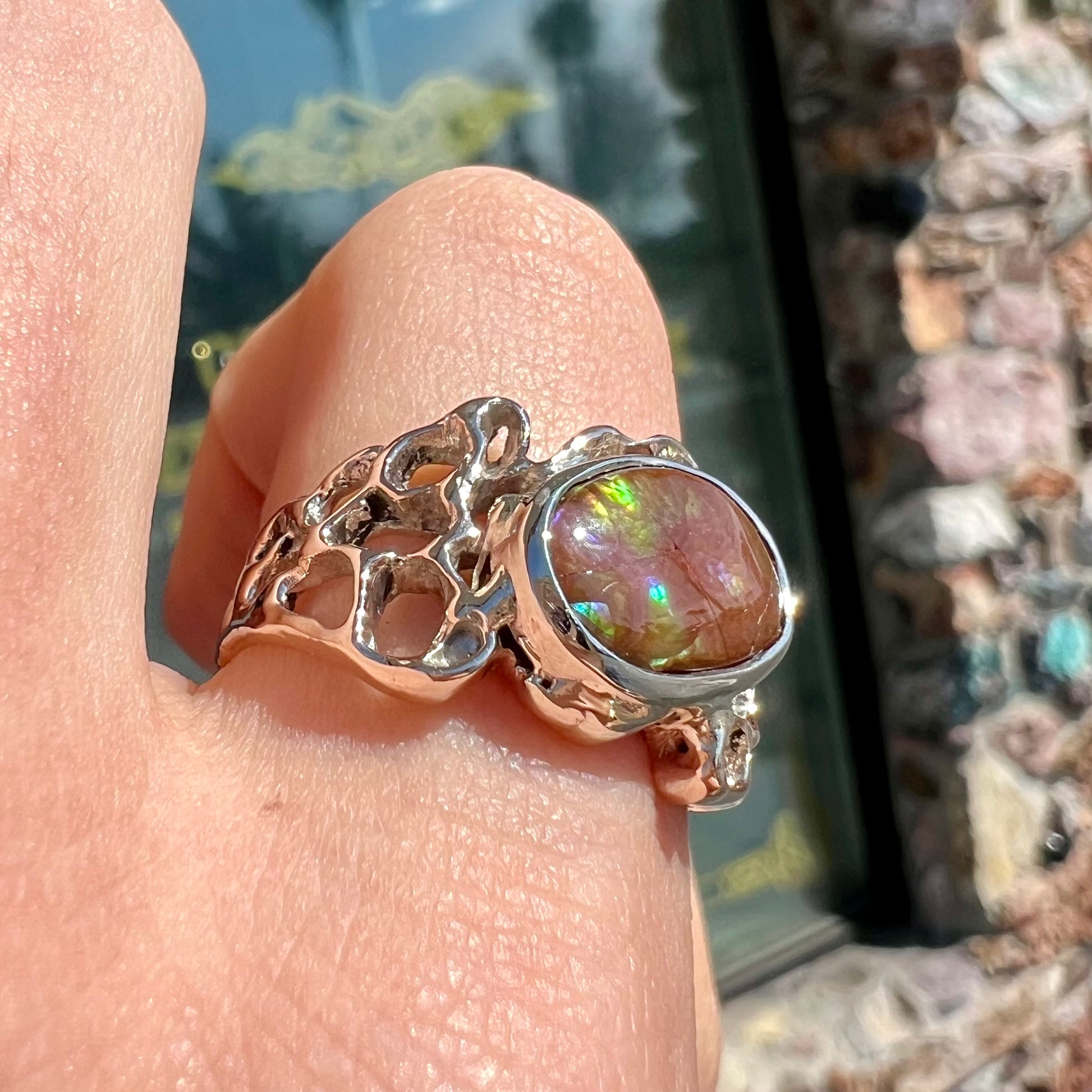 An organic-style white gold men's ring, bezel set with an oval cut Mexican fire agate stone.  The stone is green and purple.