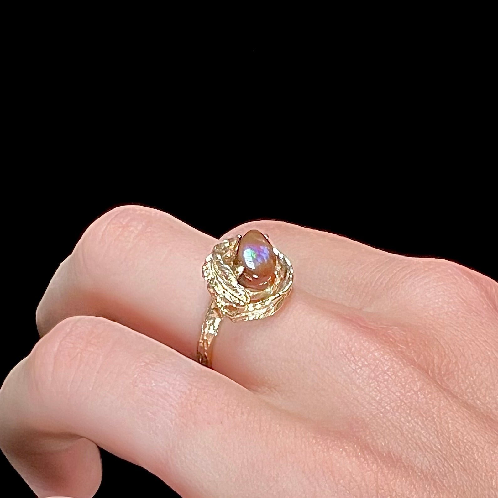 A ladies' organic style yellow gold ring set with a pear shaped cabochon cut Mexican fire agate.  The stone shines green and purple.