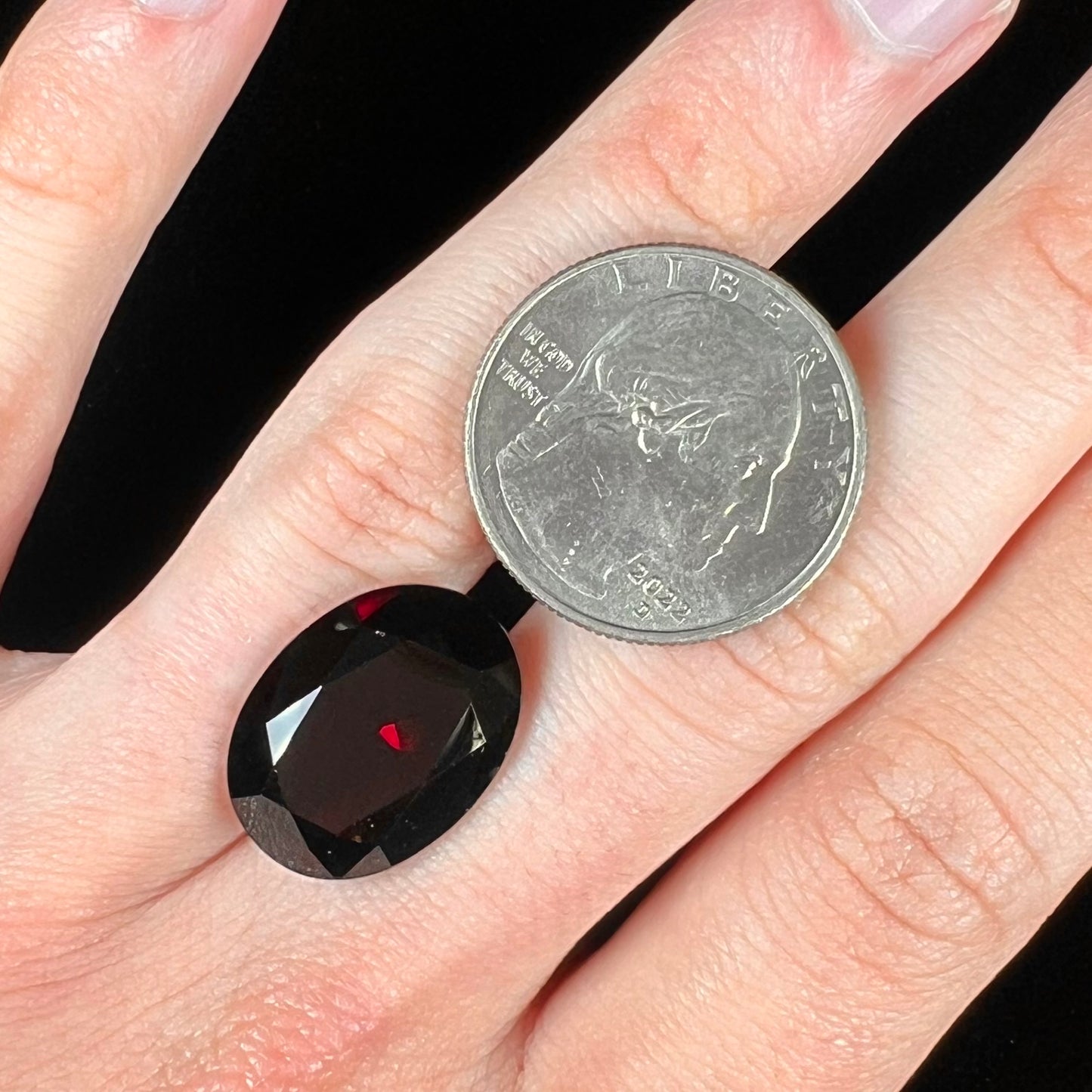 A loose, faceted oval cut pyrope garnet gemstone. The stone is a deep, dark red color.