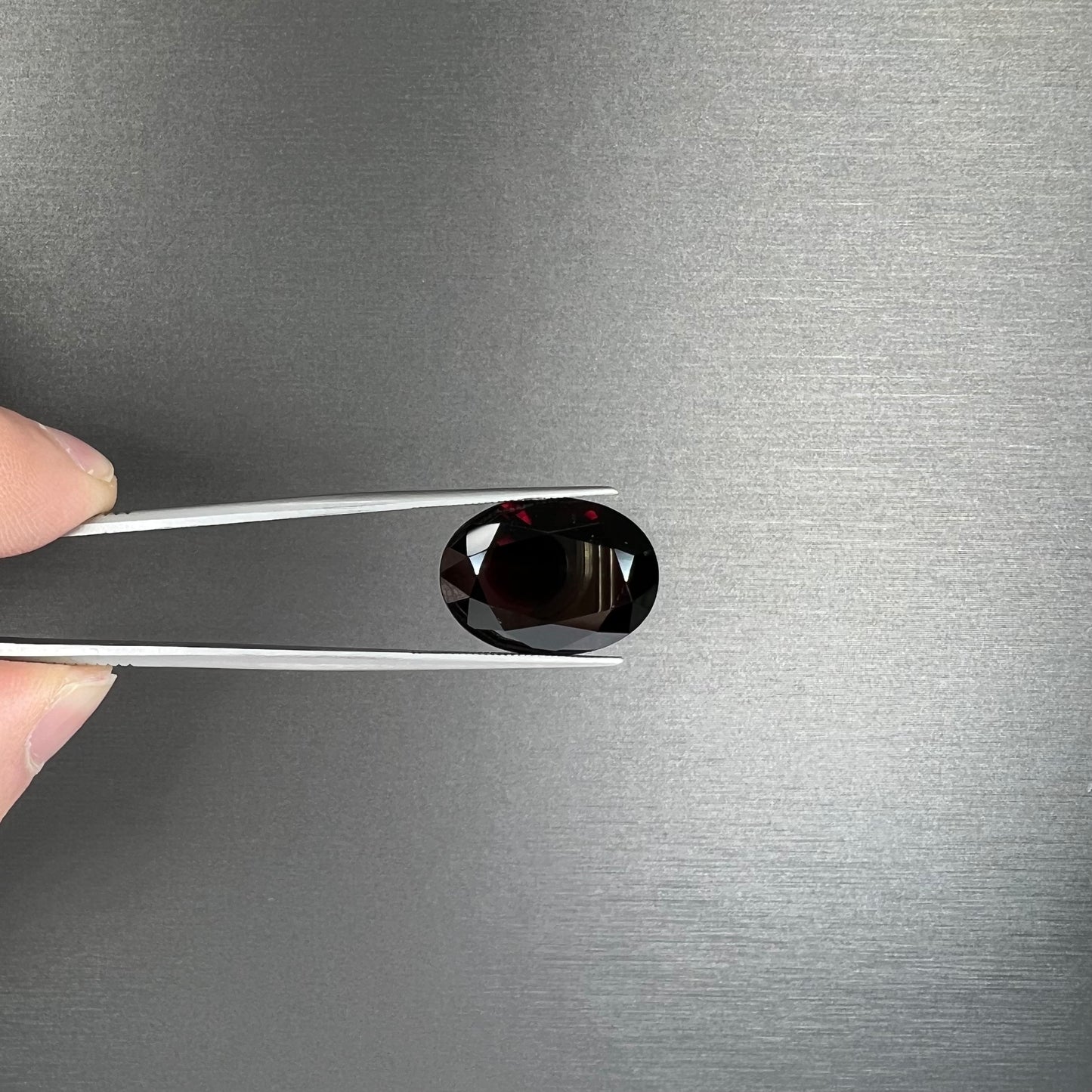 A loose, faceted oval cut pyrope garnet gemstone. The stone is a deep, dark red color.
