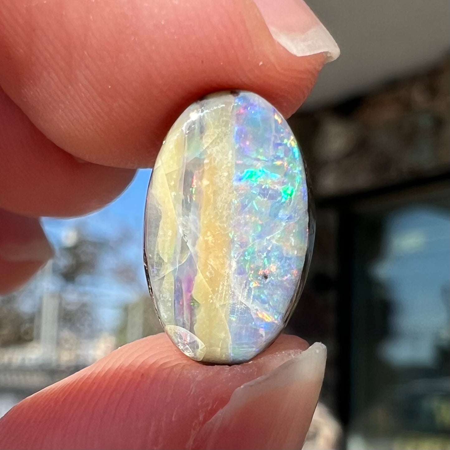 An oval cabochon cut boulder opal from Quilpie, Australia. The opal has multicolor color play.