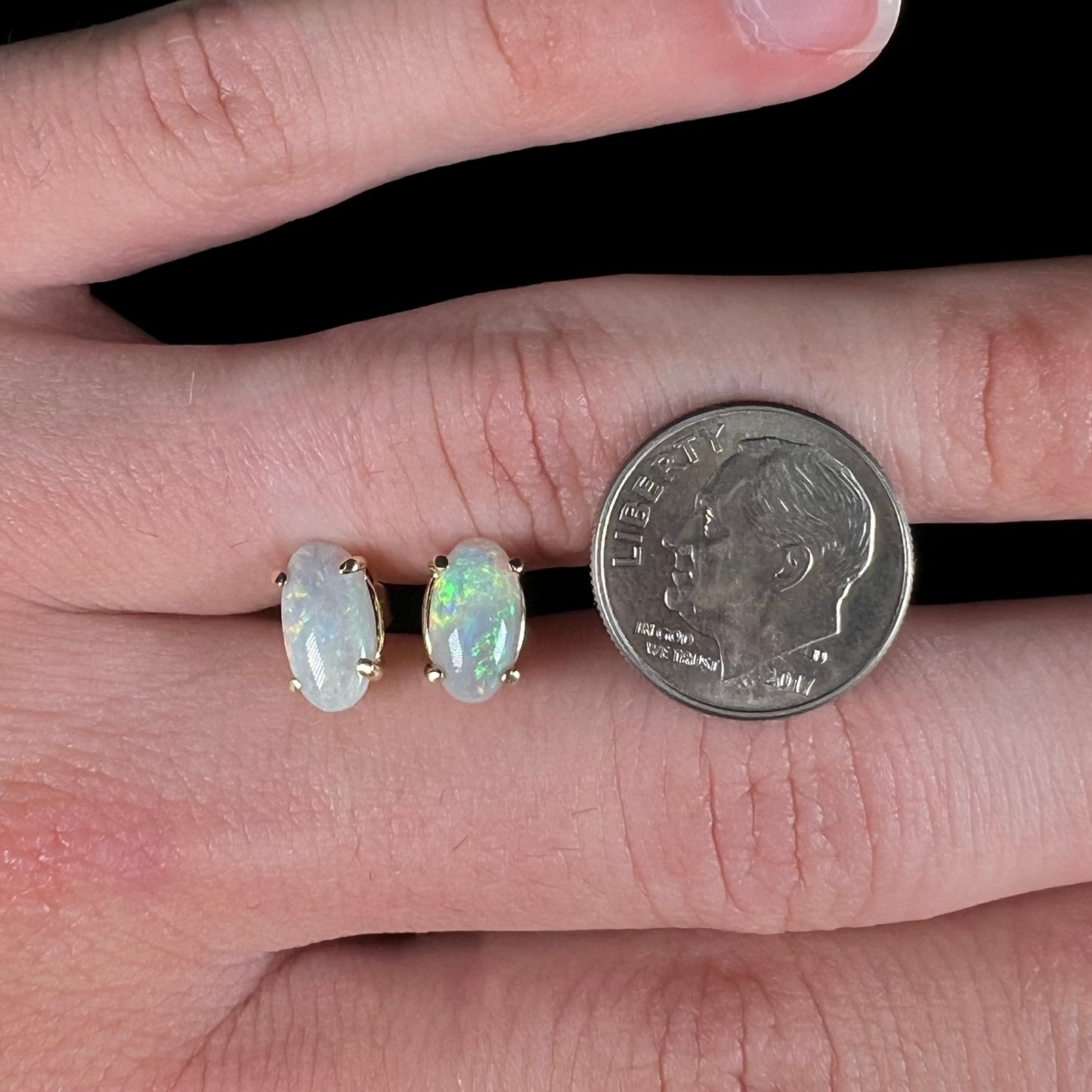A pair of natural, semi-black crystal opal stud earrings in yellow gold. The opals are oval cabochon cut.