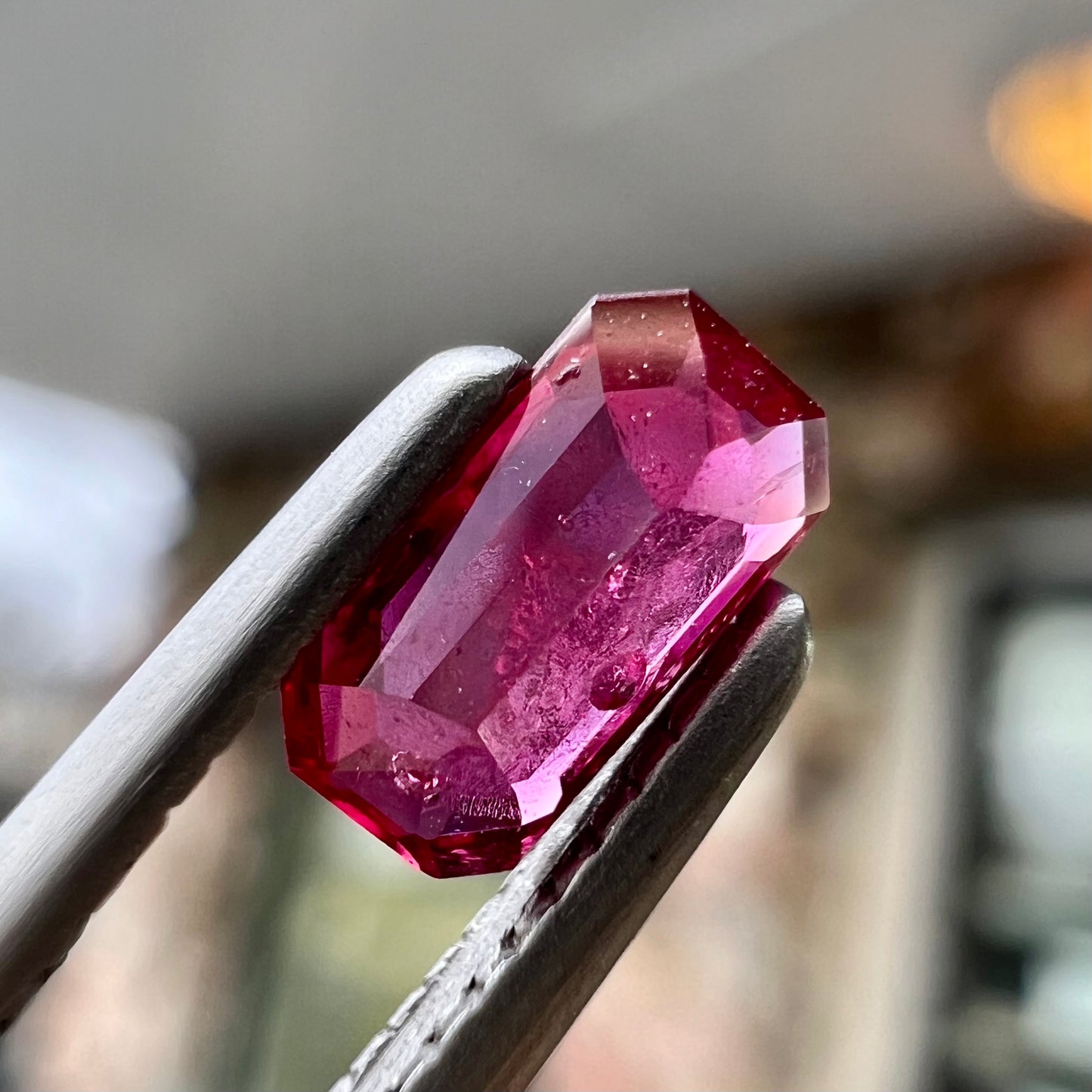 A loose, purplish red natural ruby gemstone. The stone is emerald cut.