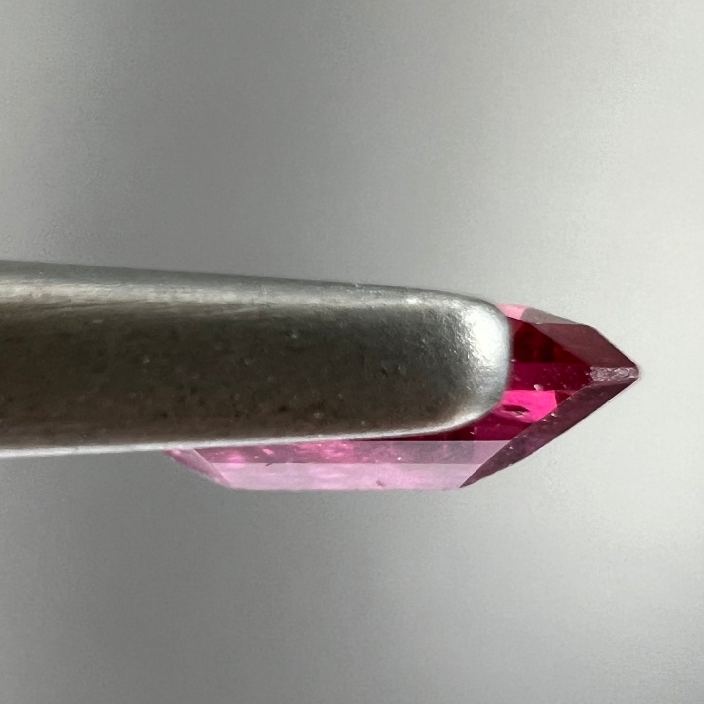 A loose, purplish red natural ruby gemstone. The stone is emerald cut.