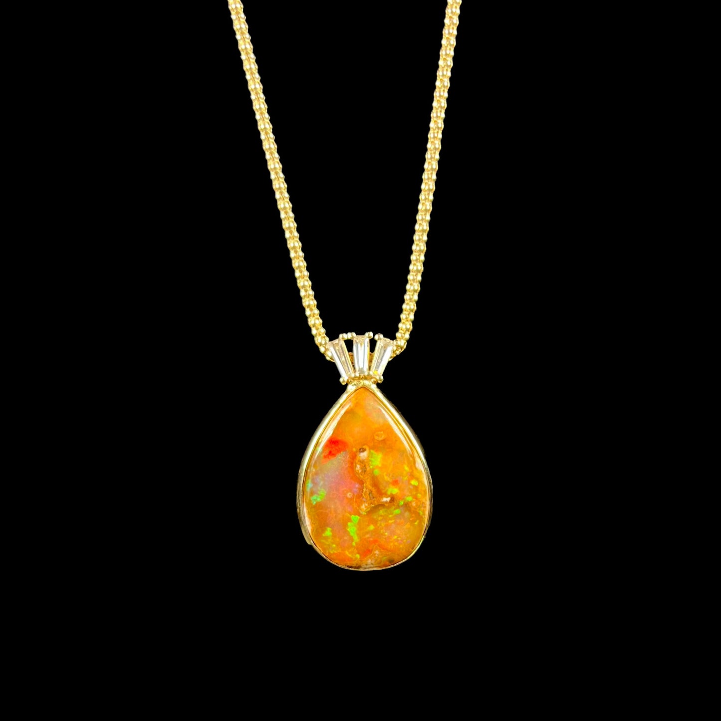 A unisex pear shaped fire opal pendant set with tapered baguette cut diamond accents in 18 karat gold.