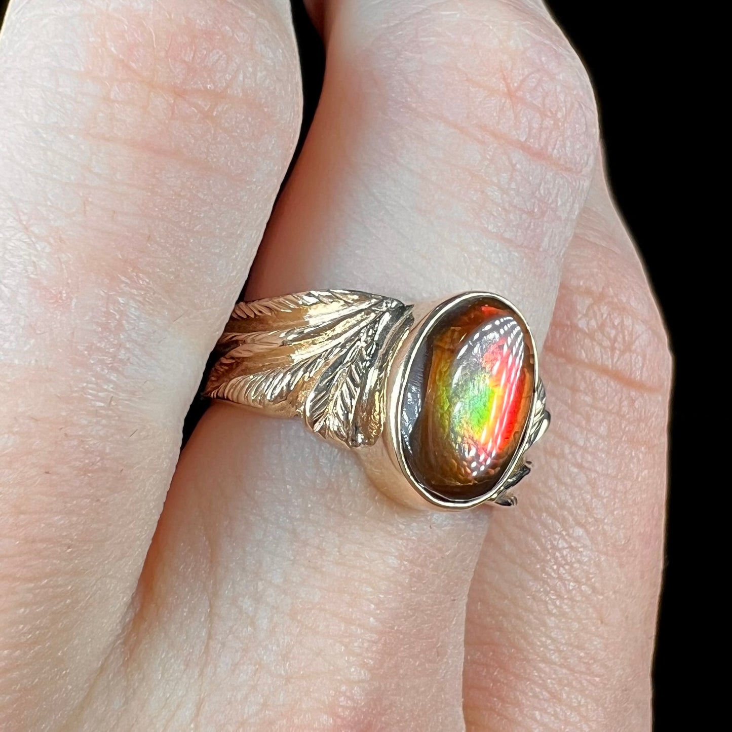 A unisex oval cabochon cut fire agate ring cast in yellow gold. The stone flashes green and red colors.