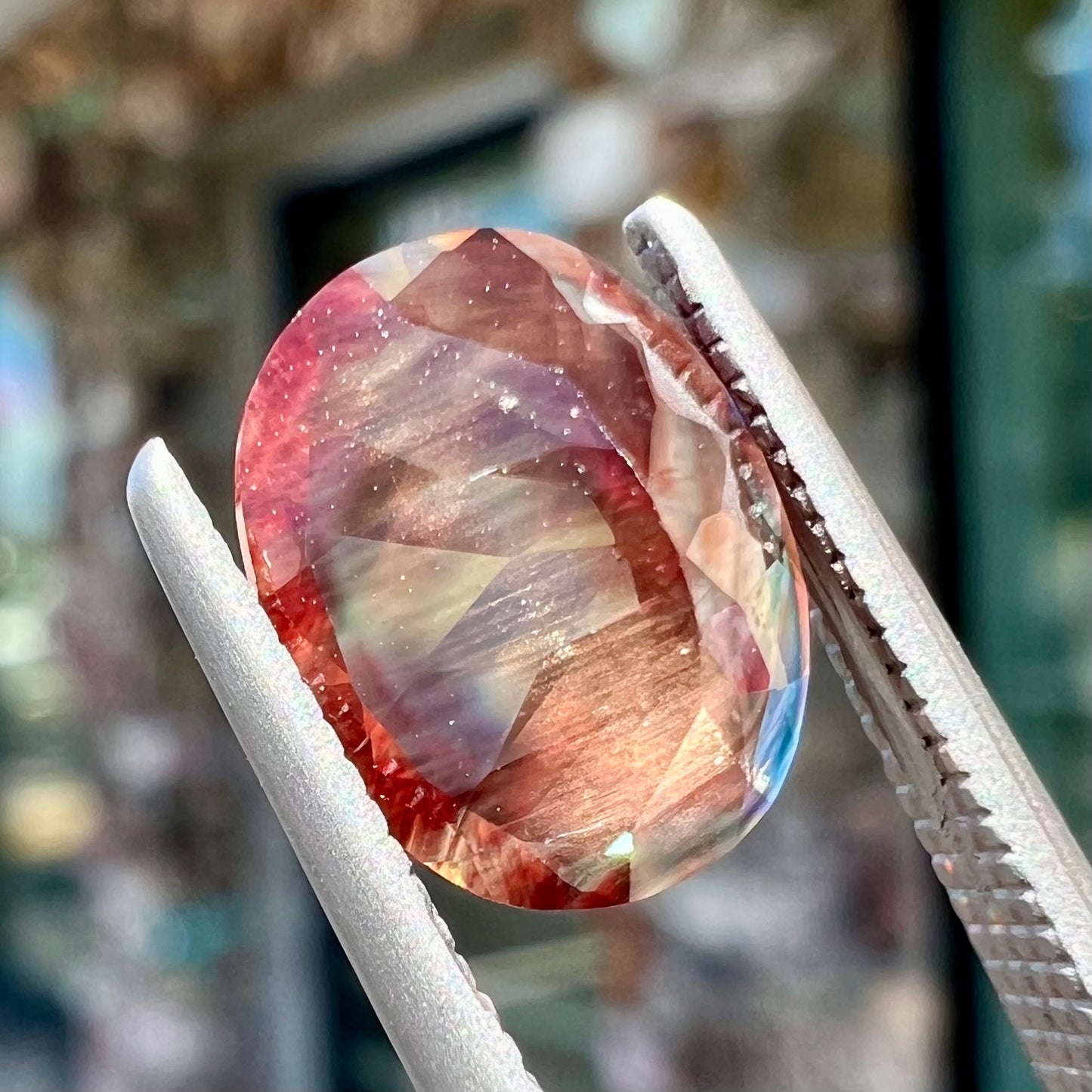 A loose, oval cut oregon sunstone.  The gem is reddish orange with a green secondary color.