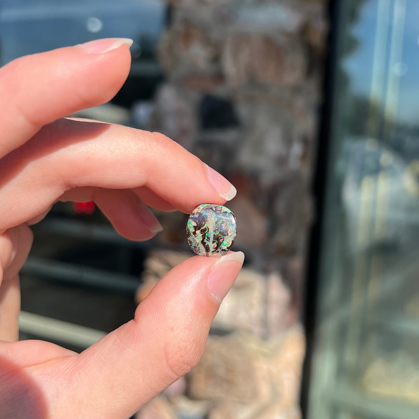 An off-round cabochon cut boulder opal stone from Koroit, Australia. The opal has green, blue, and red colors.