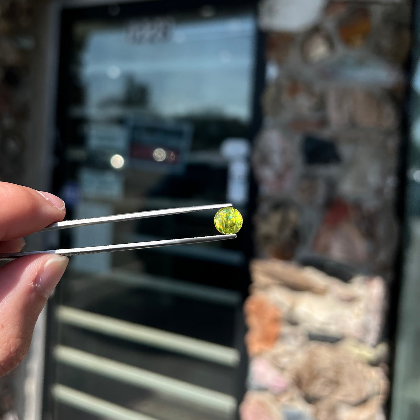 A loose, round brilliant cut sphene gemstone. The stone is green with orange, green, blue, and yellow flashes.