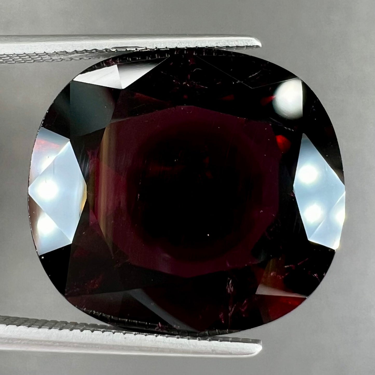 A loose, faceted oval cut rubellite tourmaline gemstone. The stone is a dark purple red color.