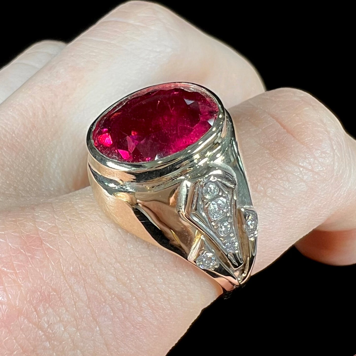 A men's yellow gold ring set with an oval cut rubellite tourmaline with diamond accents.