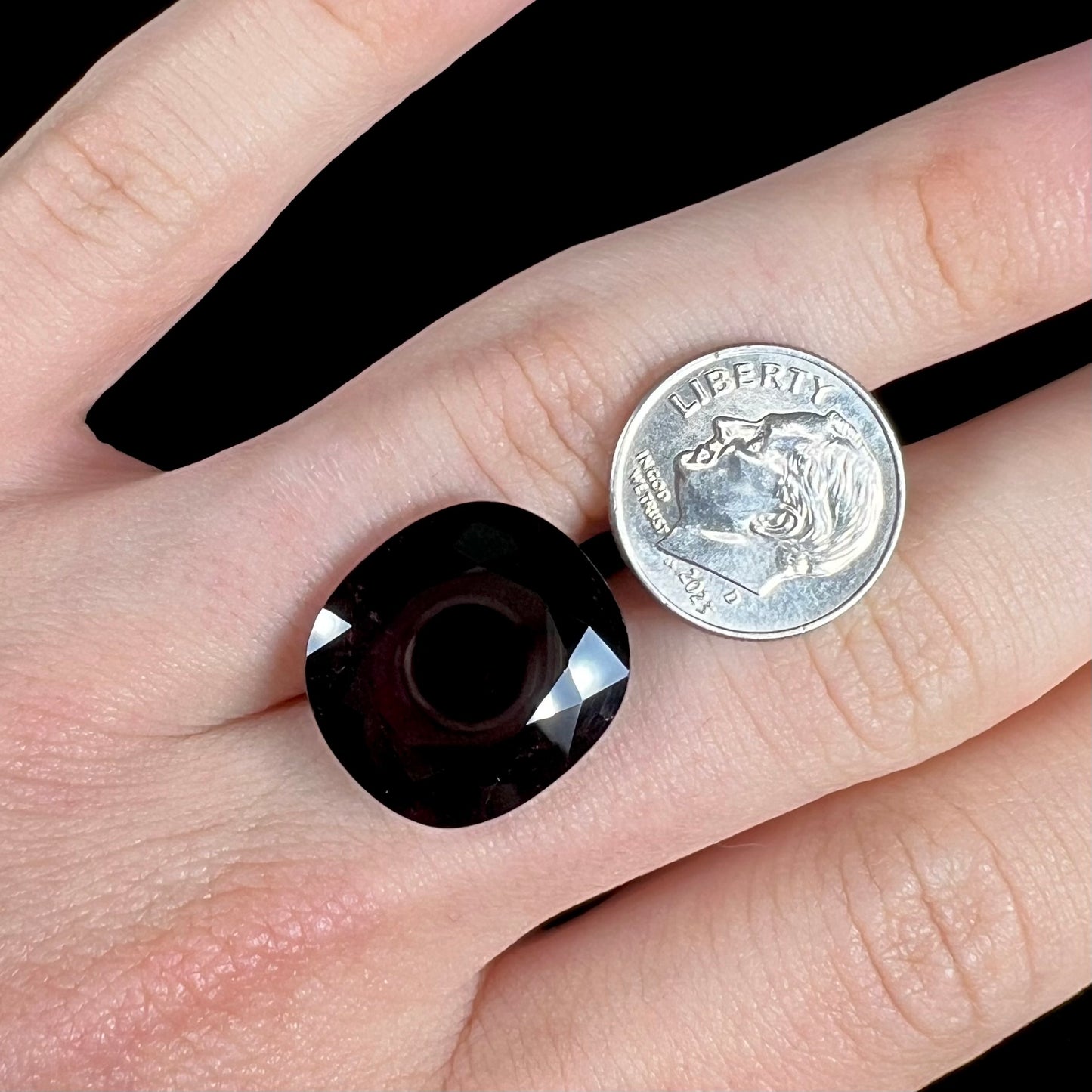 A loose, faceted oval cut rubellite tourmaline gemstone. The stone is a dark purple red color.