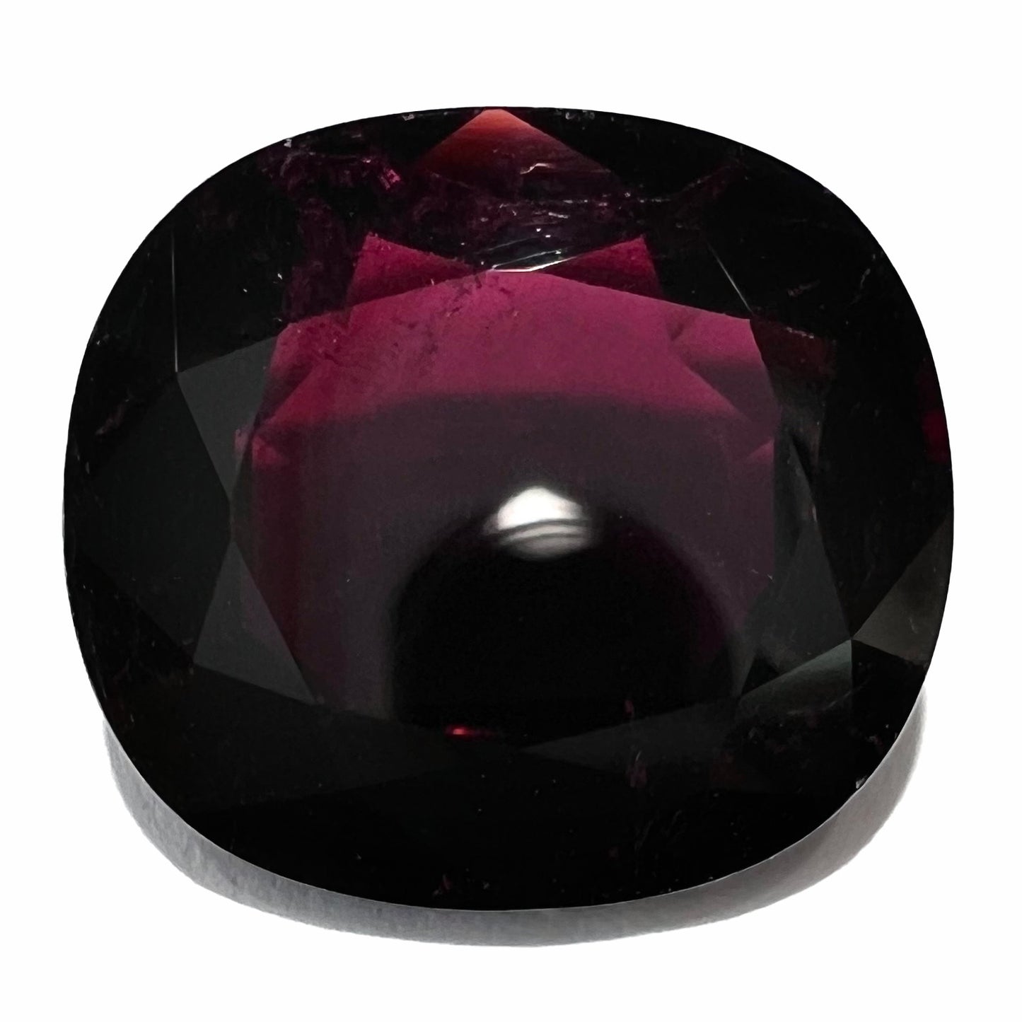 A loose, faceted oval cut rubellite tourmaline gemstone. The stone is a dark purple red color.