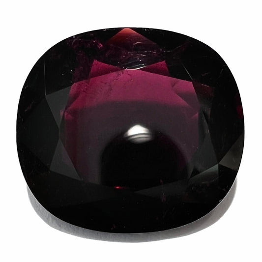 A loose, faceted oval cut rubellite tourmaline gemstone.  The stone is a dark purple red color.