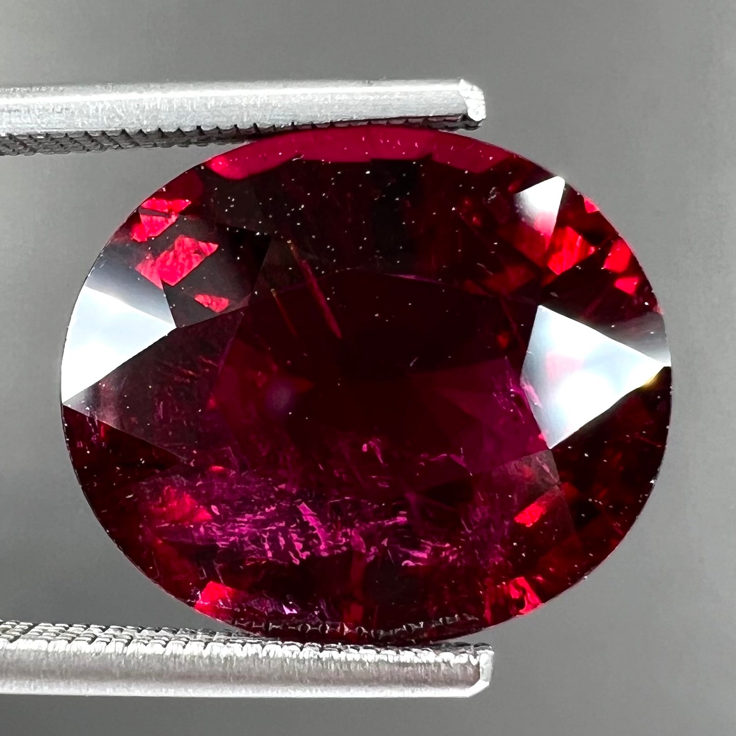 A loose, oval cut purplish red rubellite tourmaline stone.