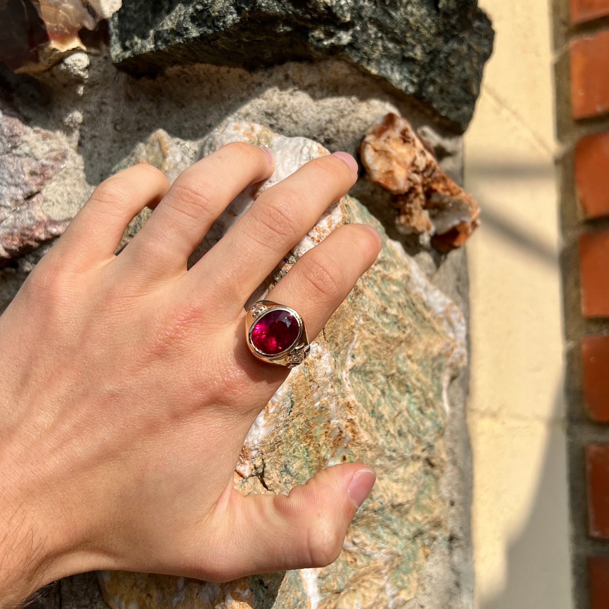 A men's yellow gold ring set with an oval cut rubellite tourmaline with diamond accents.