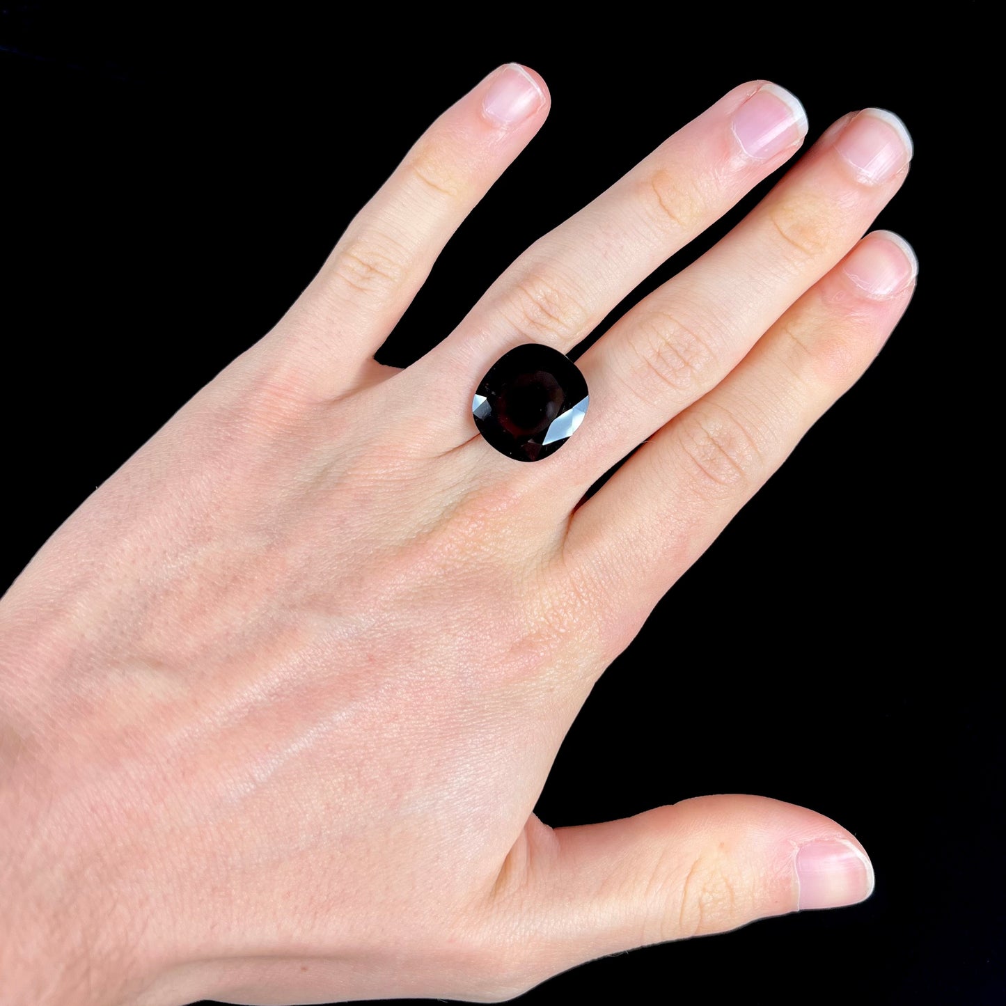 A loose, faceted oval cut rubellite tourmaline gemstone. The stone is a dark purple red color.