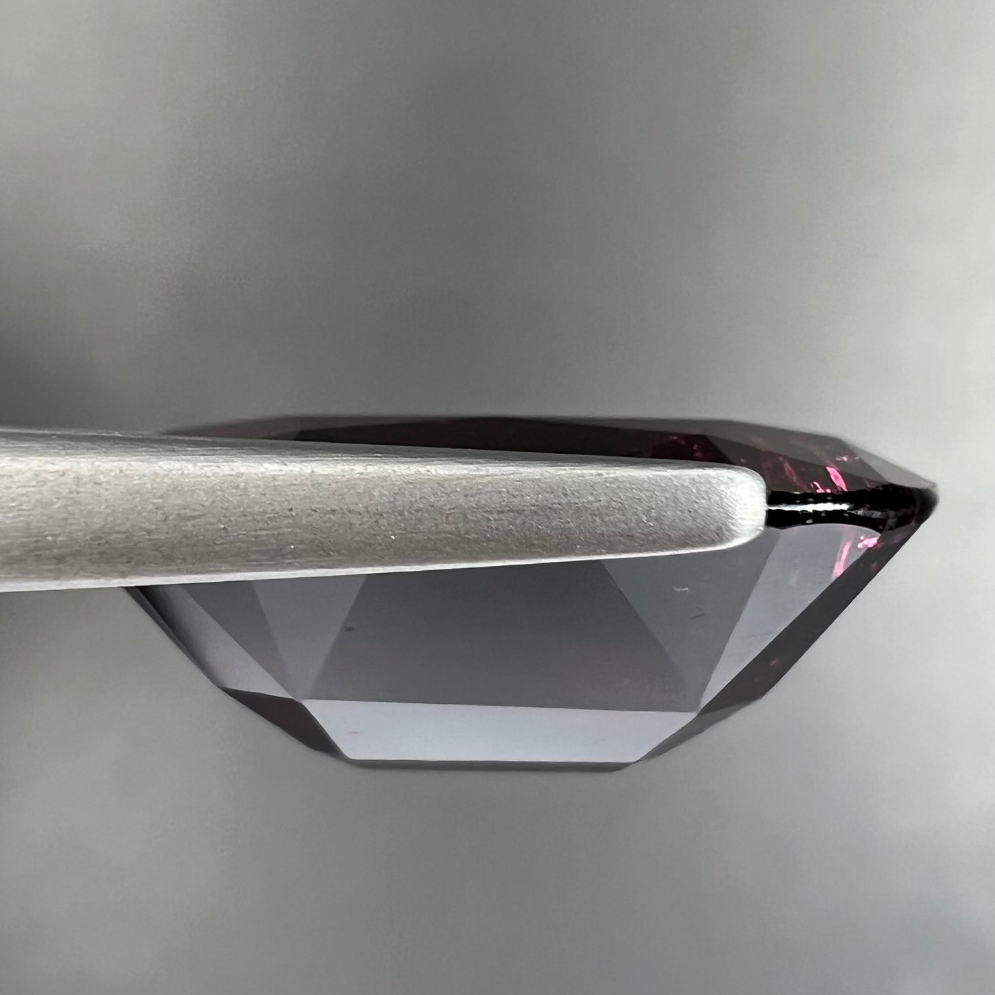 A loose, faceted oval cut rubellite tourmaline gemstone. The stone is a dark purple red color.