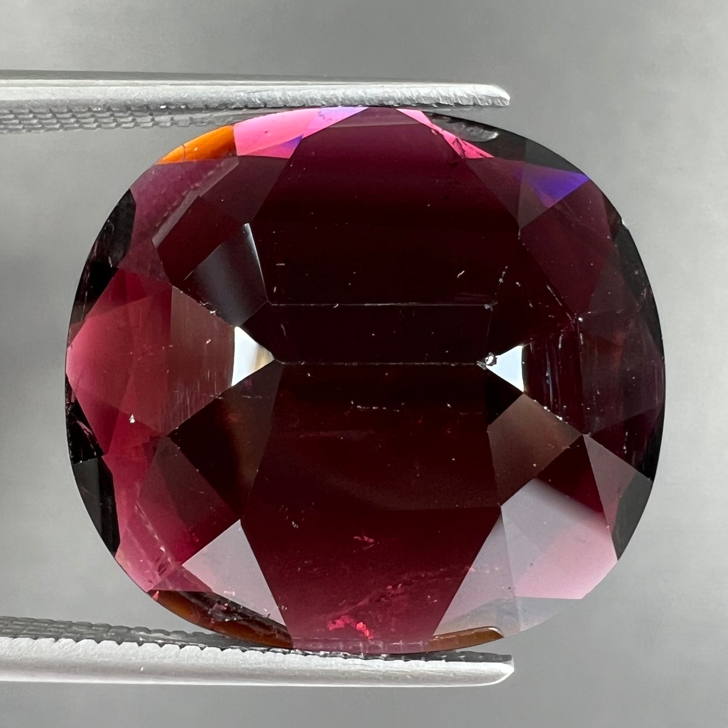 A loose, faceted oval cut rubellite tourmaline gemstone. The stone is a dark purple red color.