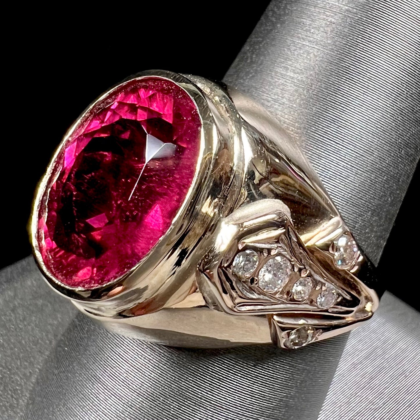 A men's yellow gold ring set with an oval cut rubellite tourmaline with diamond accents.