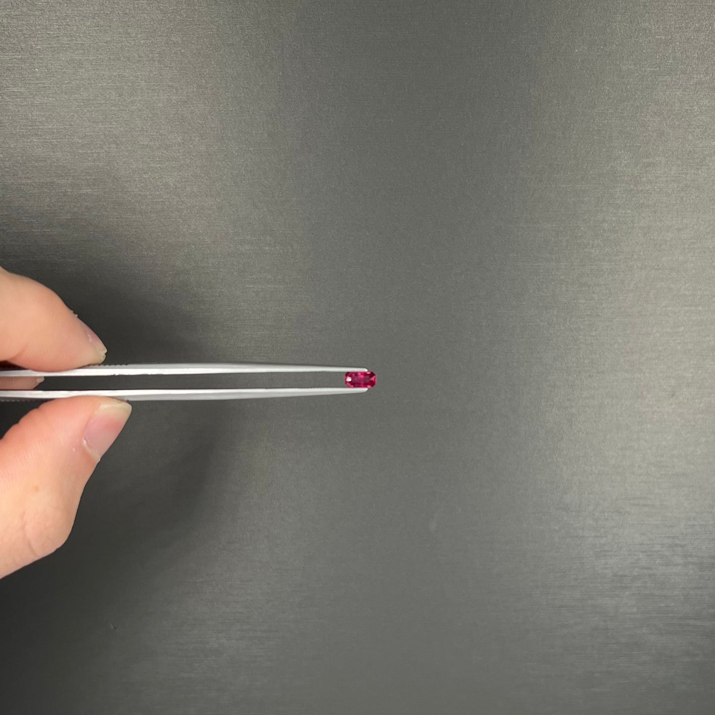 A loose, purplish red natural ruby gemstone. The stone is emerald cut.