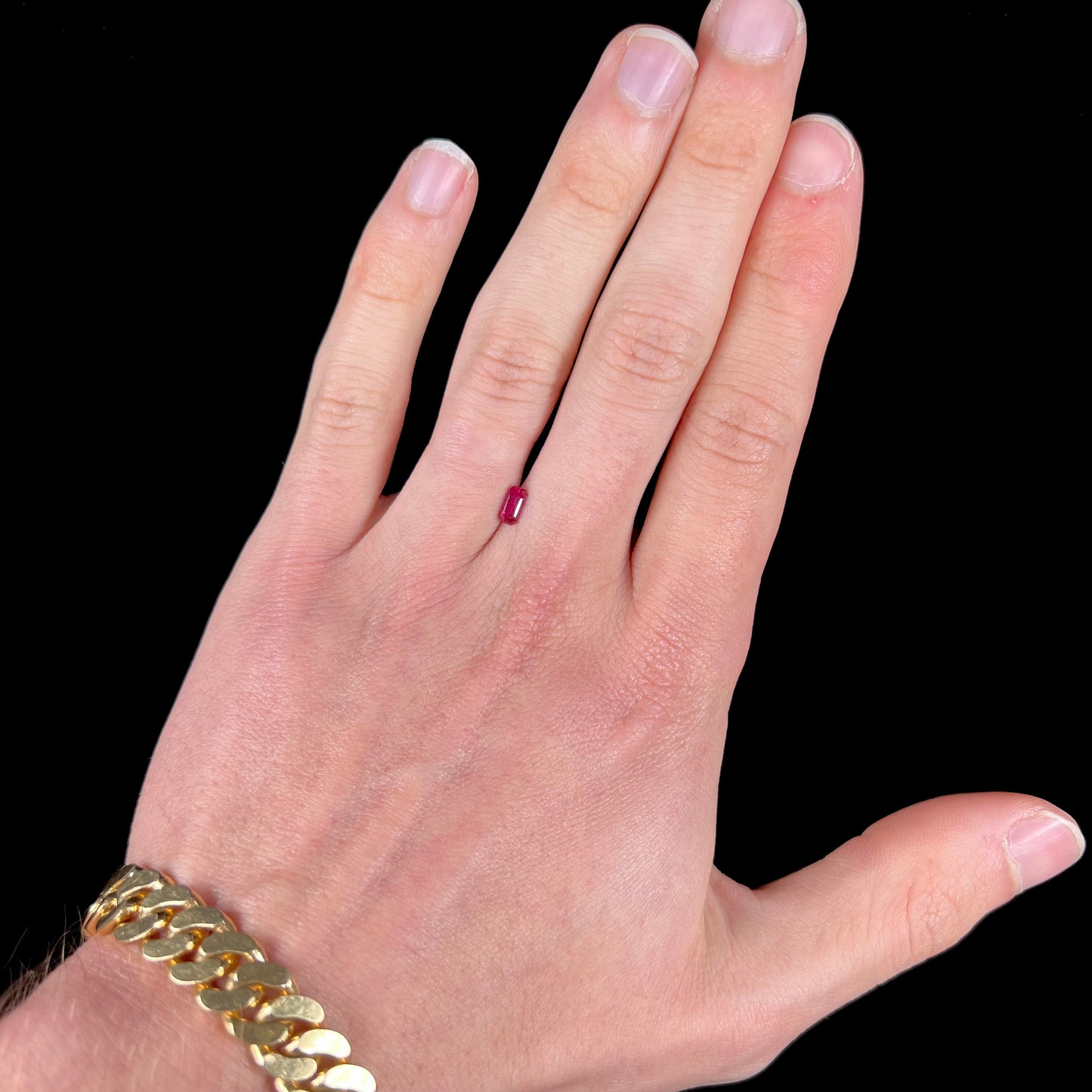 A loose, purplish red natural ruby gemstone. The stone is emerald cut.