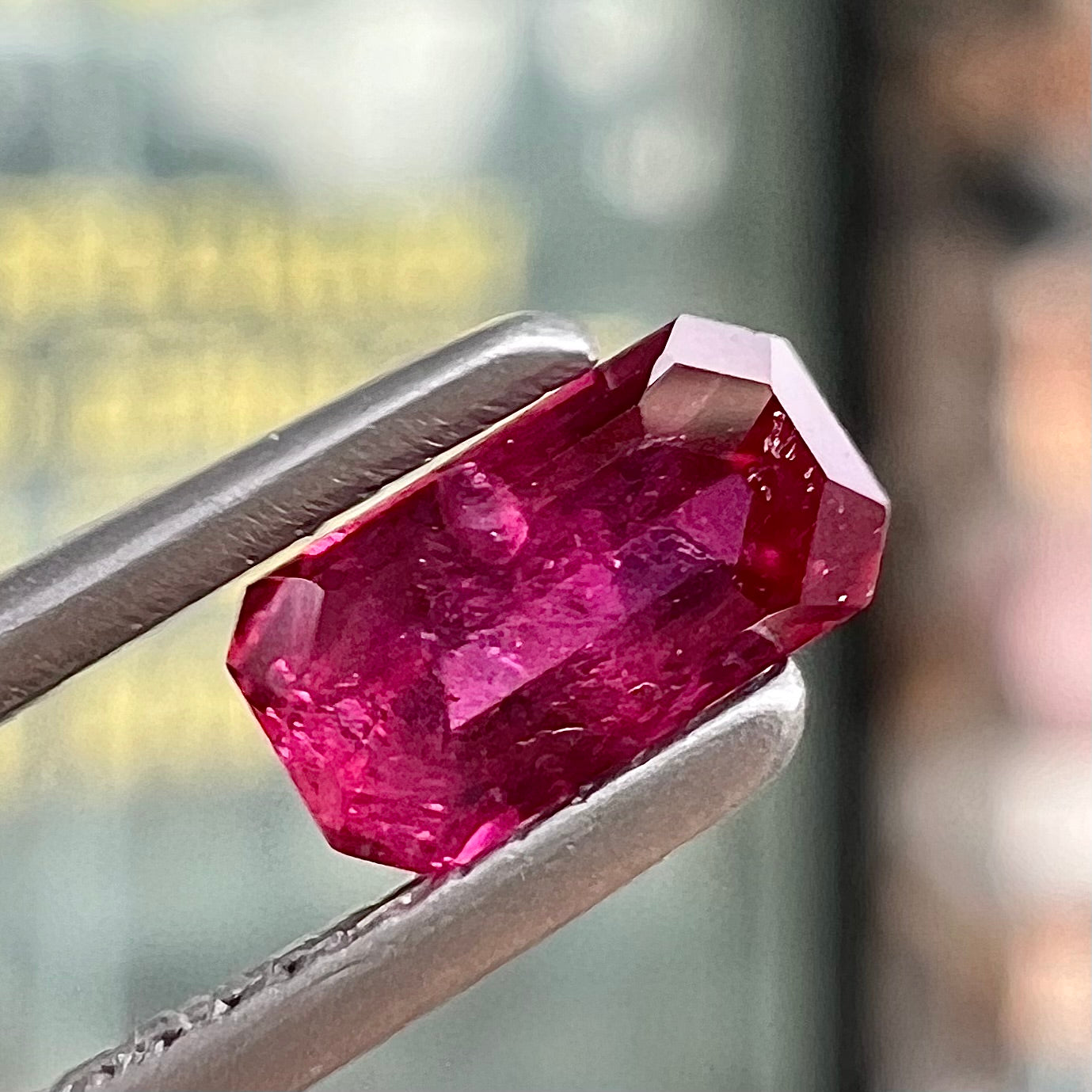 A loose, purplish red natural ruby gemstone. The stone is emerald cut.