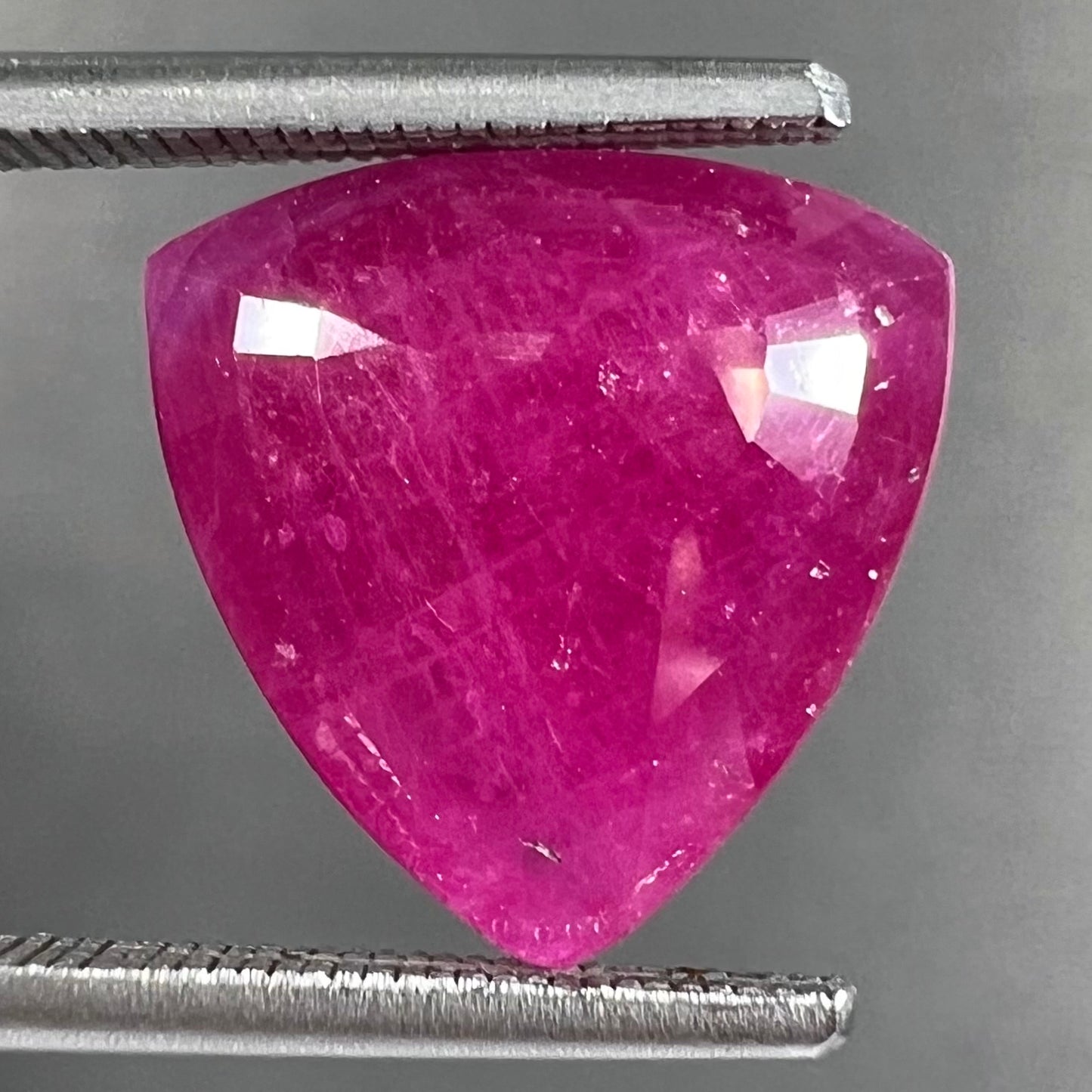 A loose, faceted trillion cut, natural, commercial grade ruby gemstone. The stone is purplish red color.