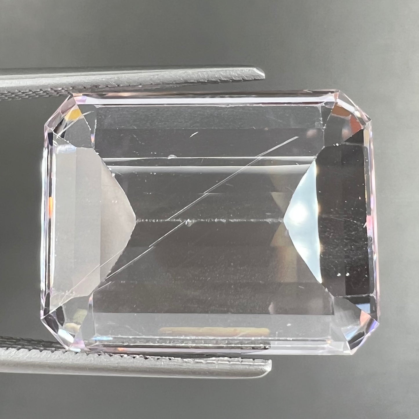 A loose, emerald cut kunzite gemstone. The stone has eye-visible rutile needle inclusions and the table is abraded.
