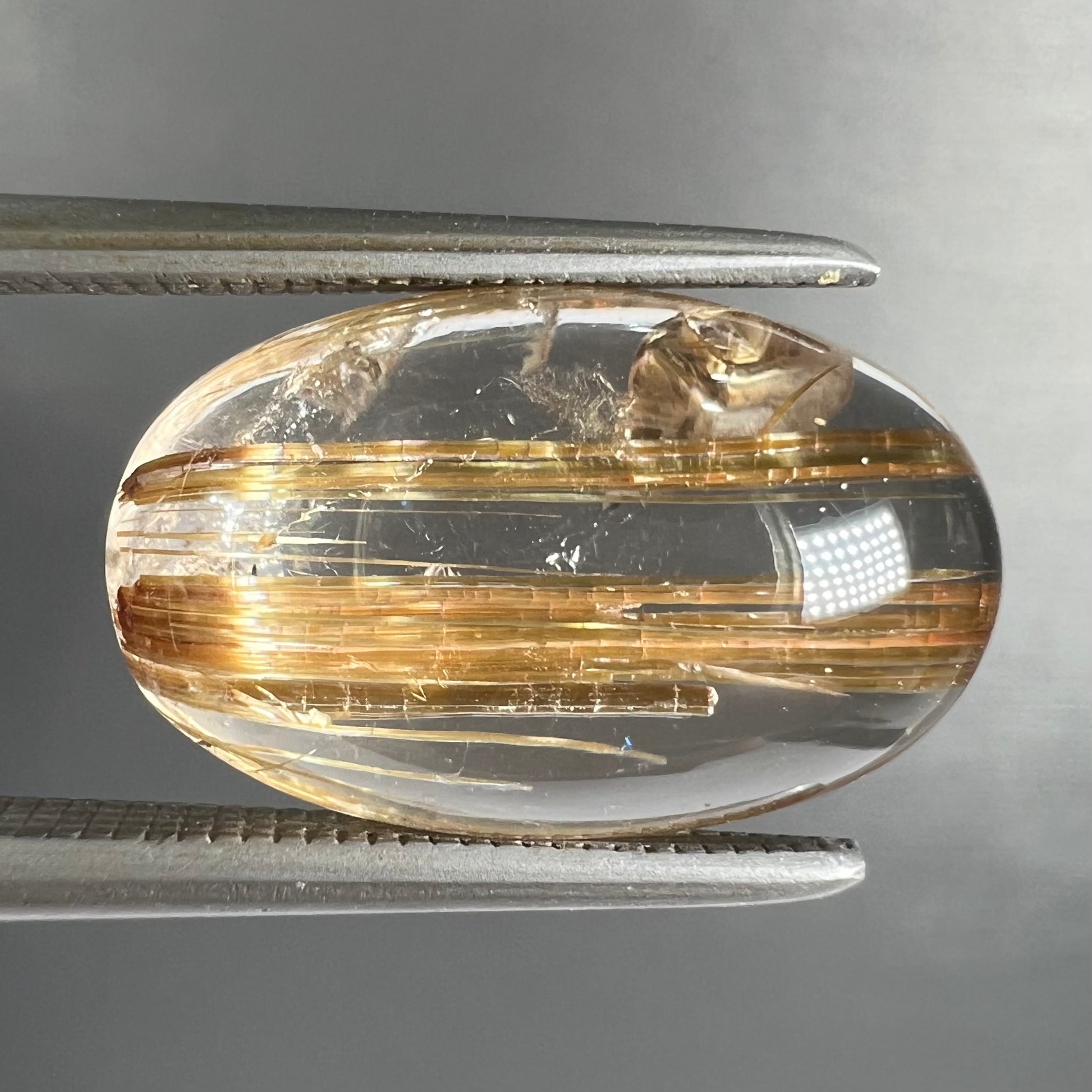 A loose, oval cabochon cut cat's eye golden rutilated quartz stone.